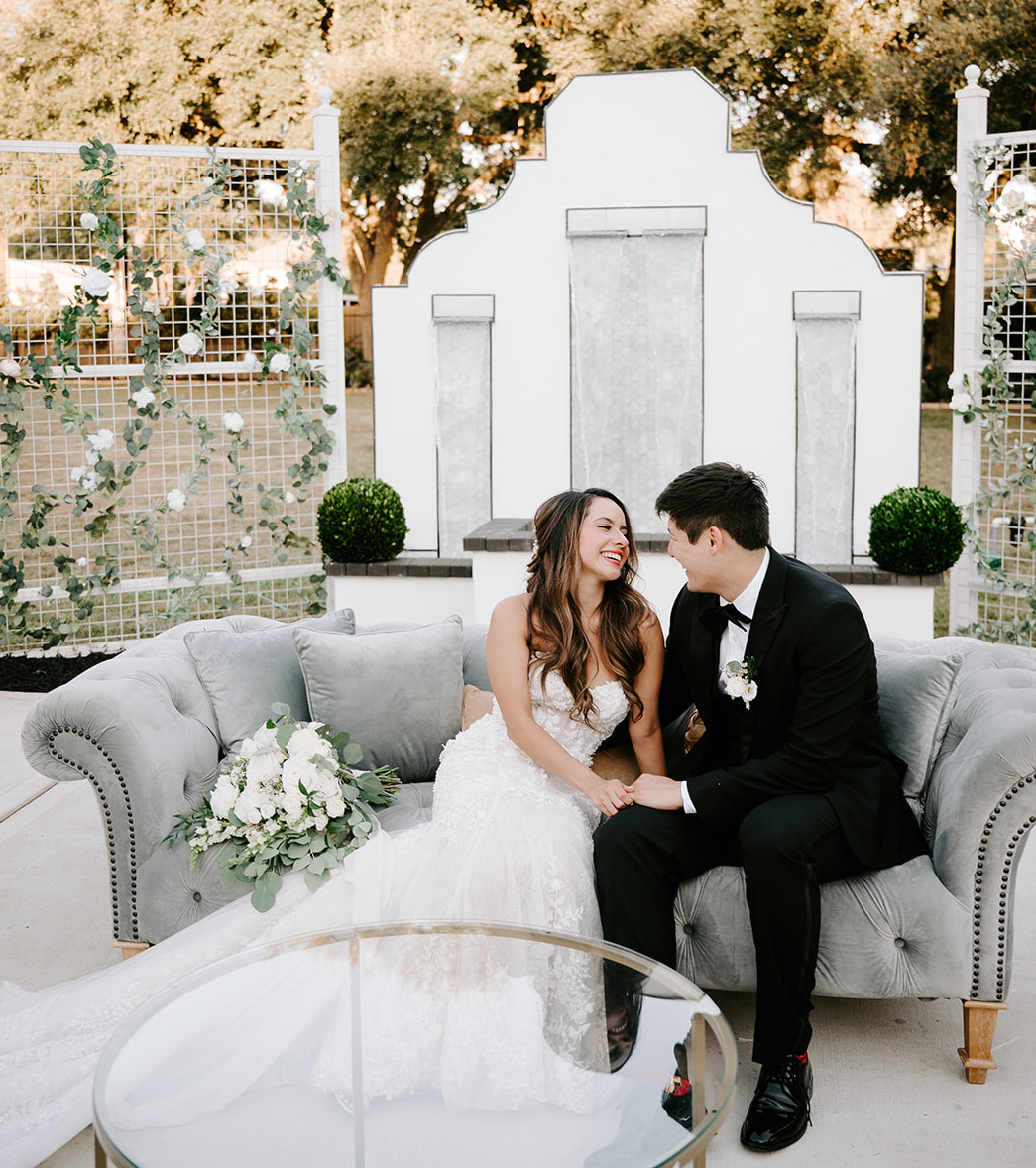 The bride and groom sit on a couch outside of their wedding venue in The Woodlands, TX.