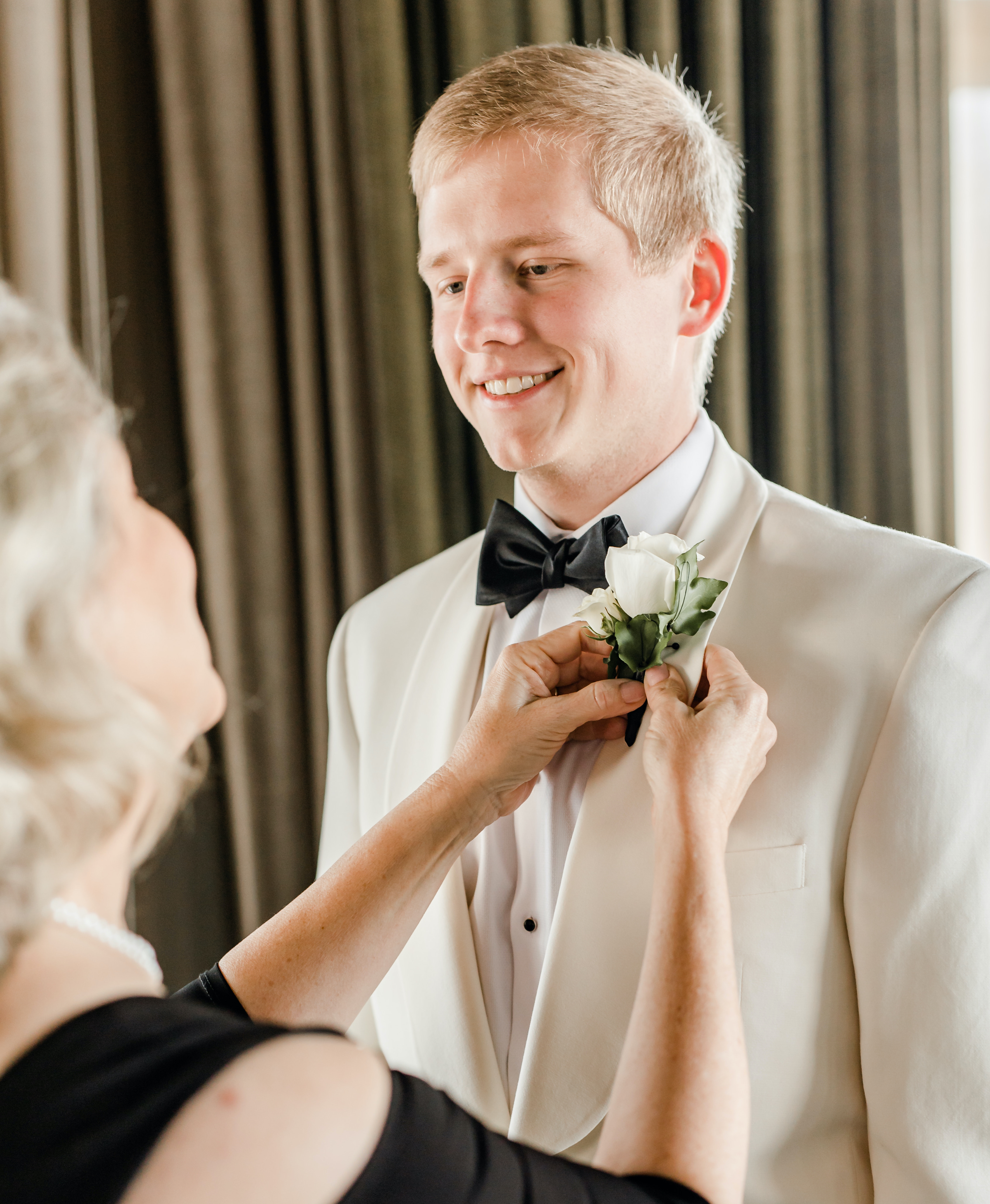 The groom's mother puts on his boutonnière while he smiles back at her before his wedding in the museum district in Houston, TX. 