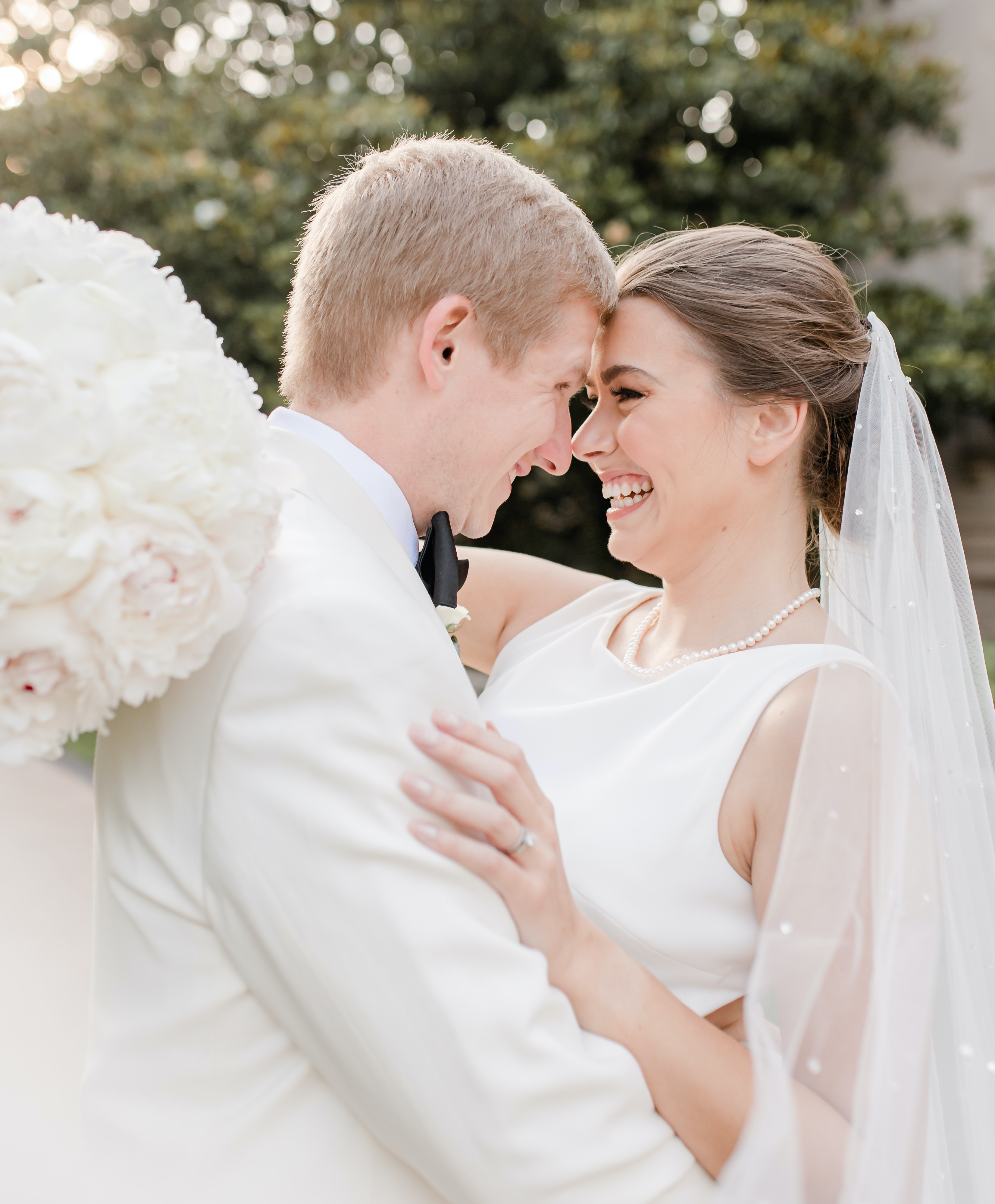 The bride and groom look each other in the eyes and hug while the bride holds her bridal bouquet behind him. They are in the Houston museum district.