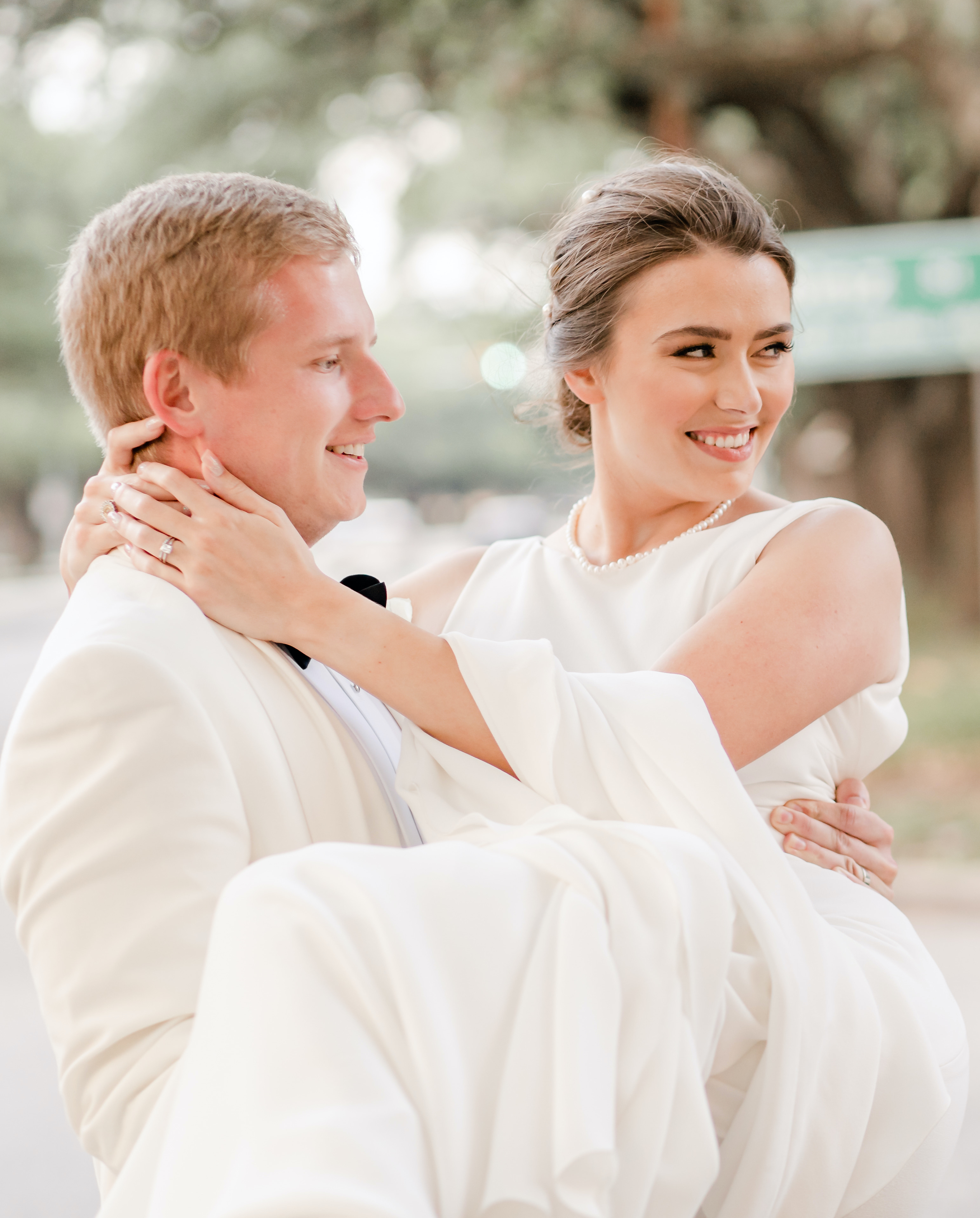 The groom holds his bride in his arms as they are both smiling in the Houston museum district.