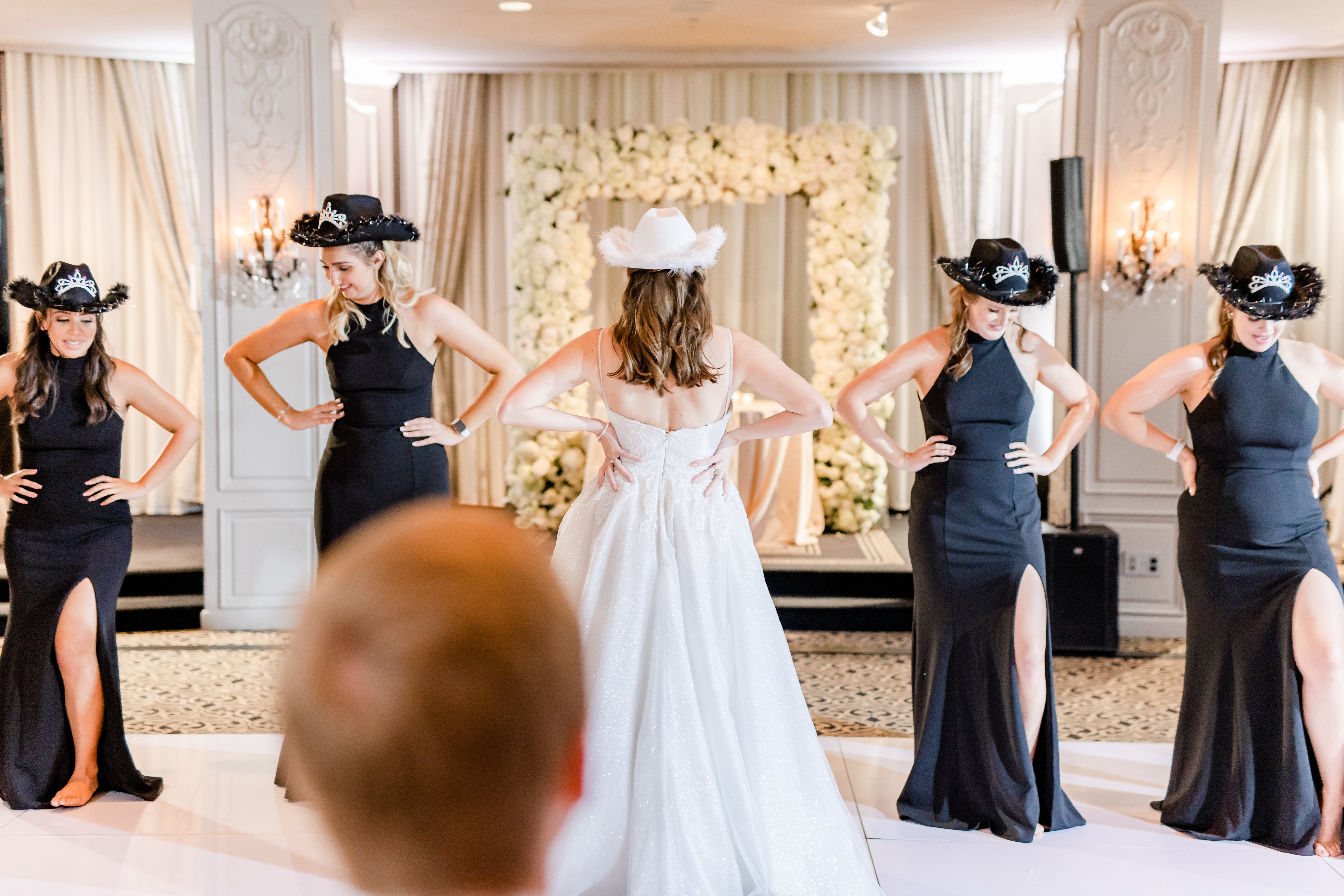 The bride performs a dance with her bridesmaids at her wedding reception. They are all wearing cowgirl hats with crowns in the Houston museum district.