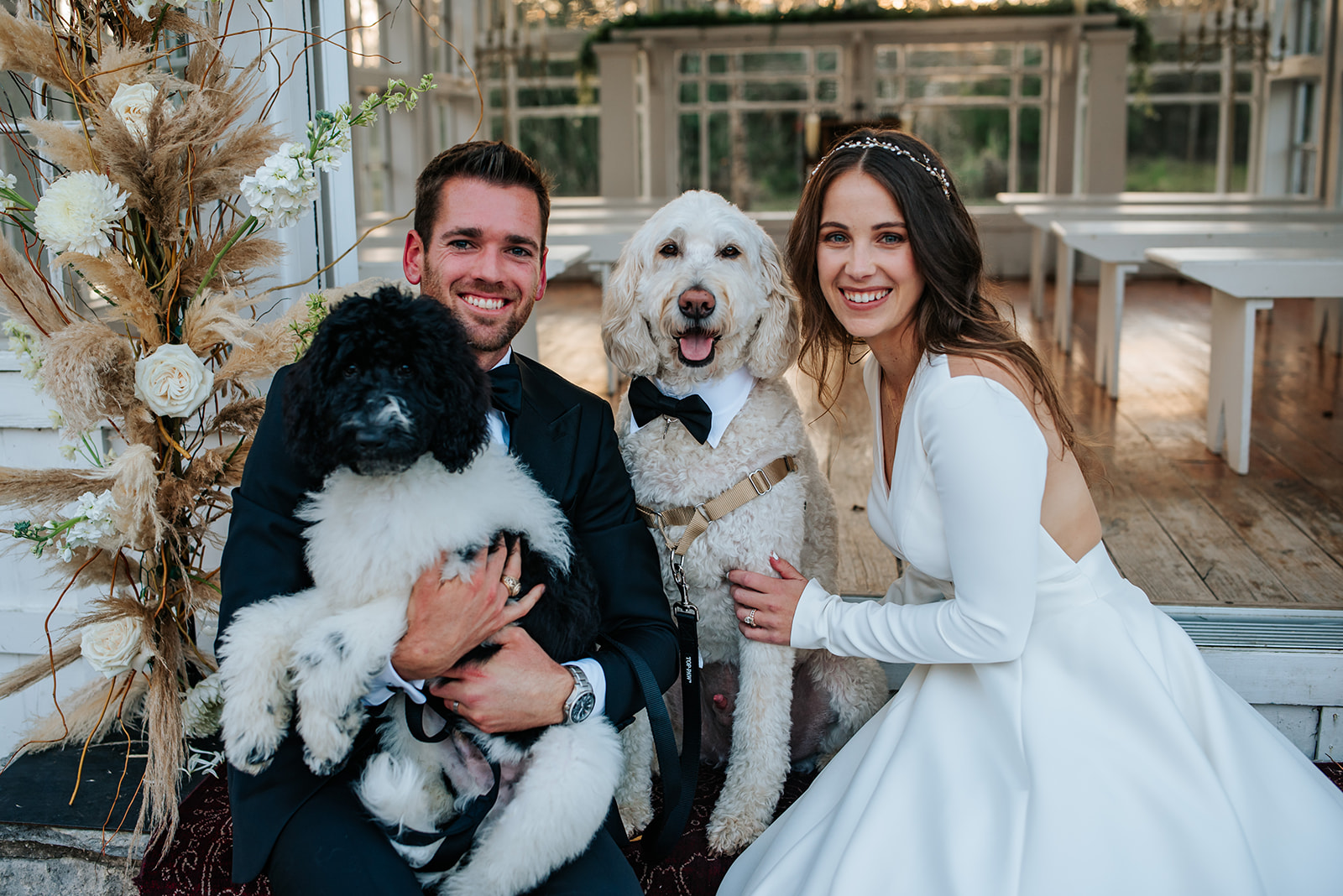 The bride and groom smile and sit with their two dogs outside on the altar after their winter wedding in Aggieland at 7F Lodge.