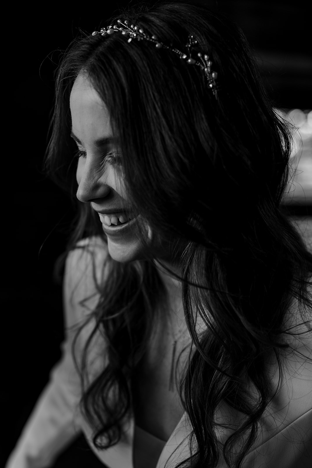 A black and white photo of the bride laughing. Her hair is loosely curled and she has a dainty flower crown in her hair.