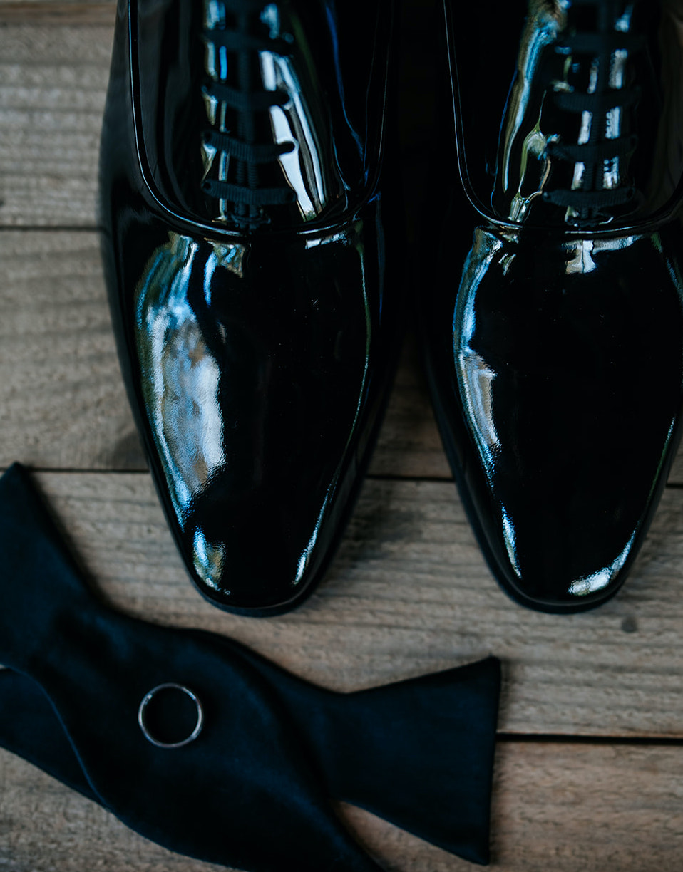 A flat lay of the groom's shoes and wedding band are placed on a wooden floor at 7F Lodge in College Station, TX.