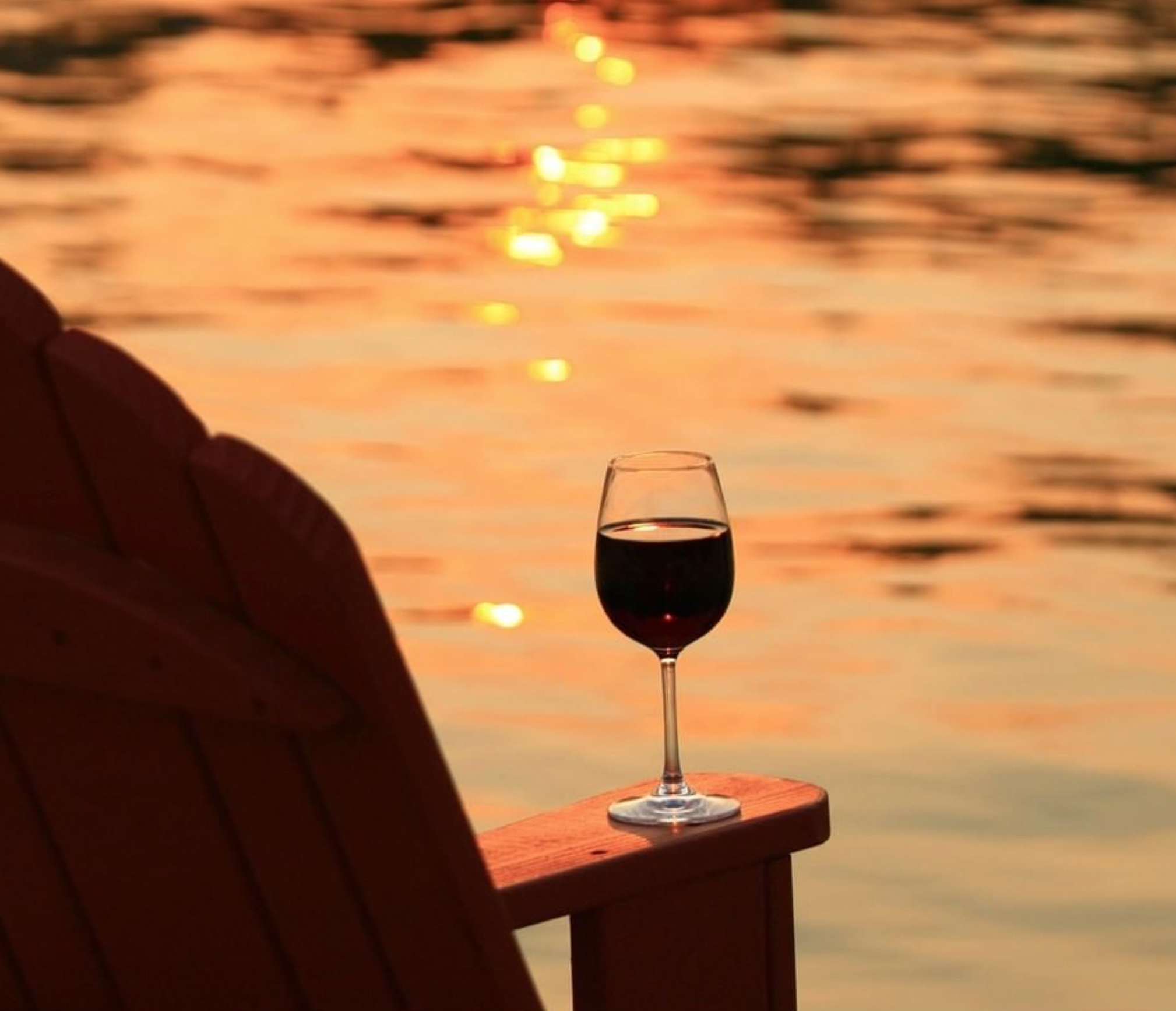 A orange and yellow sunset reflecting onto the water on Lake Conroe at the Margaritaville Lake Resort. A glass of wine sits on a lawn chair.