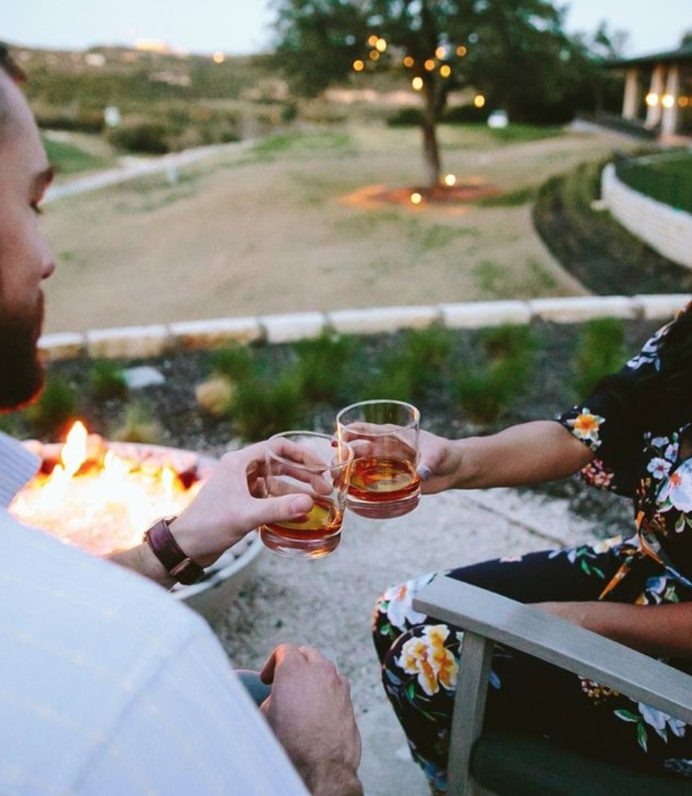 A couple cheers their drinks while sitting outside by a fire at Omni Barton Creek Resort & Spa in the Texas Hill Country.