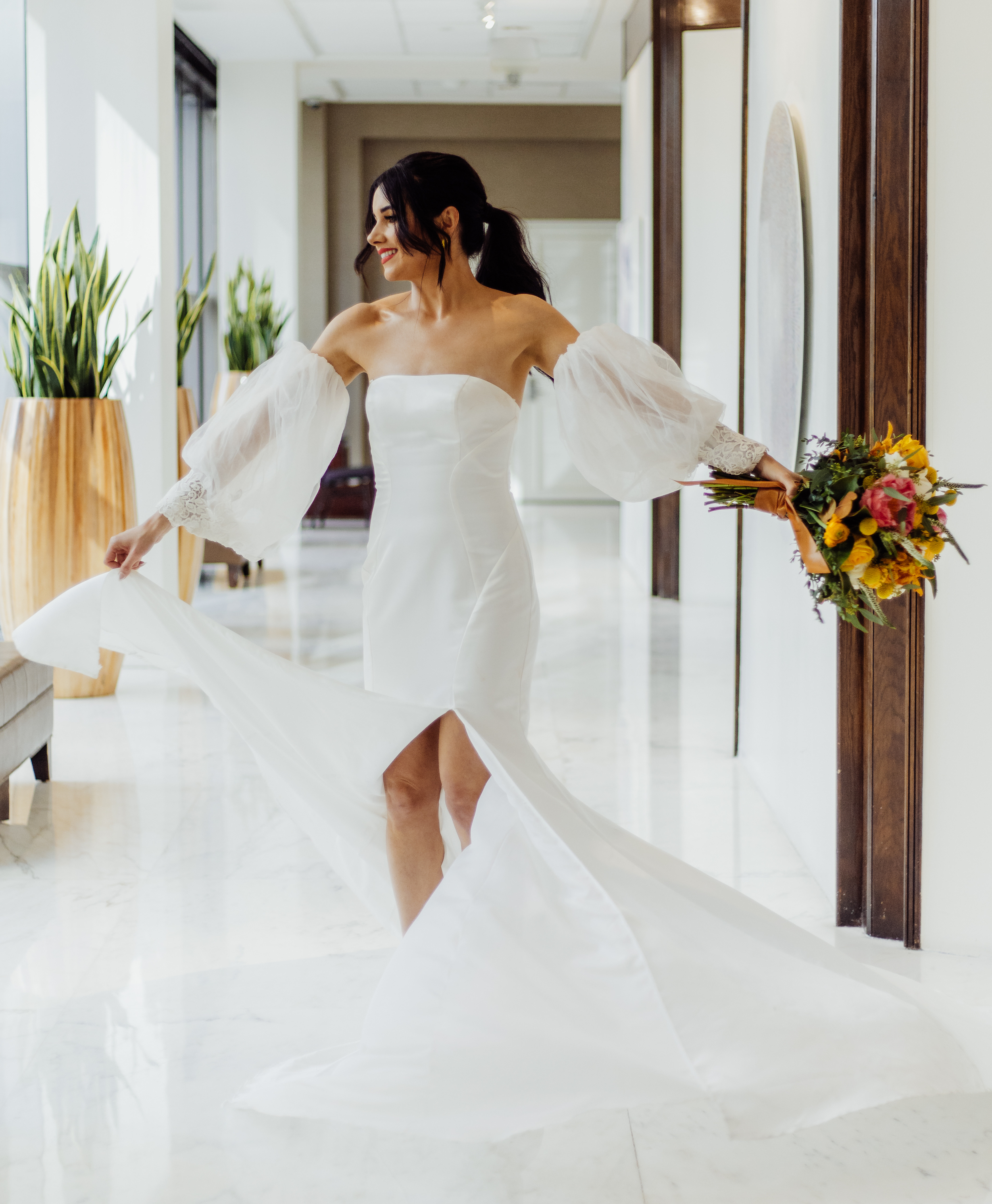 A bride twirls in the hallway at The Whitehall holding her colorful yellow and magenta bouquet.