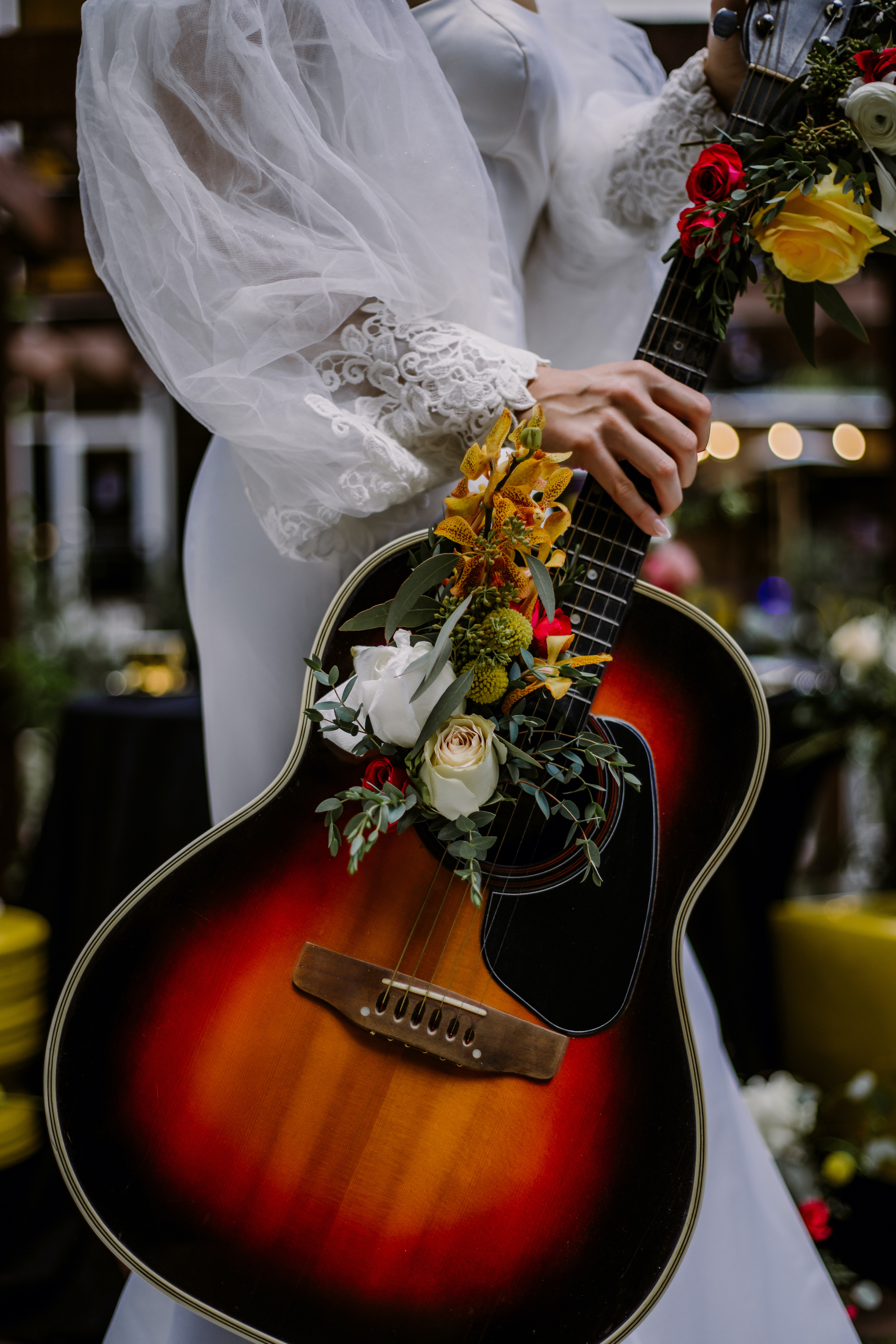 Bride in fitted white wedding gown holds a guitar wrapped with flowers outside of White Hall Hotel.