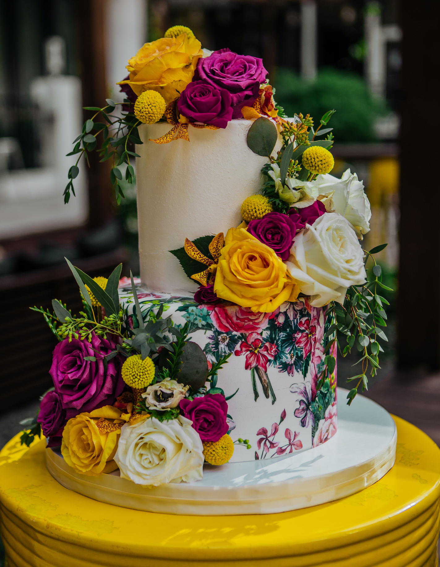 A two-tier wedding cake with vibrant yellow and magenta flowers by Common Bond Bistro and Bakery.