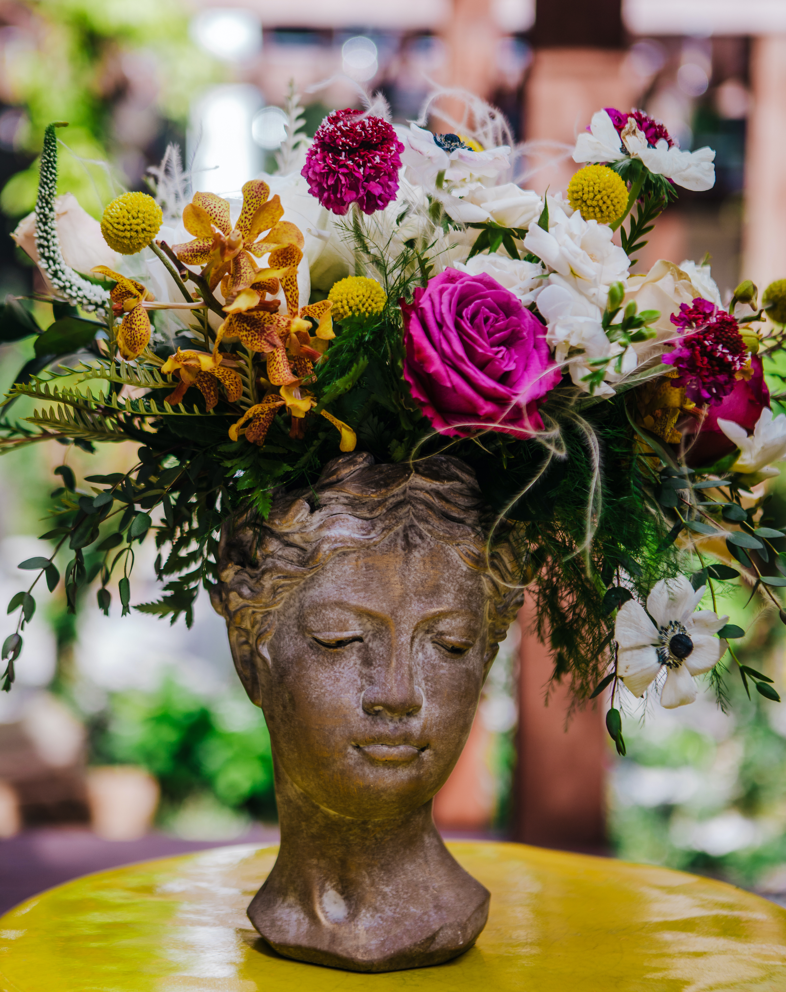 A vibrant flower arrangement of yellow, magenta and white blooms in a cement bust vase at The White Hall hotel wedding venue in downtown Houston, TX.