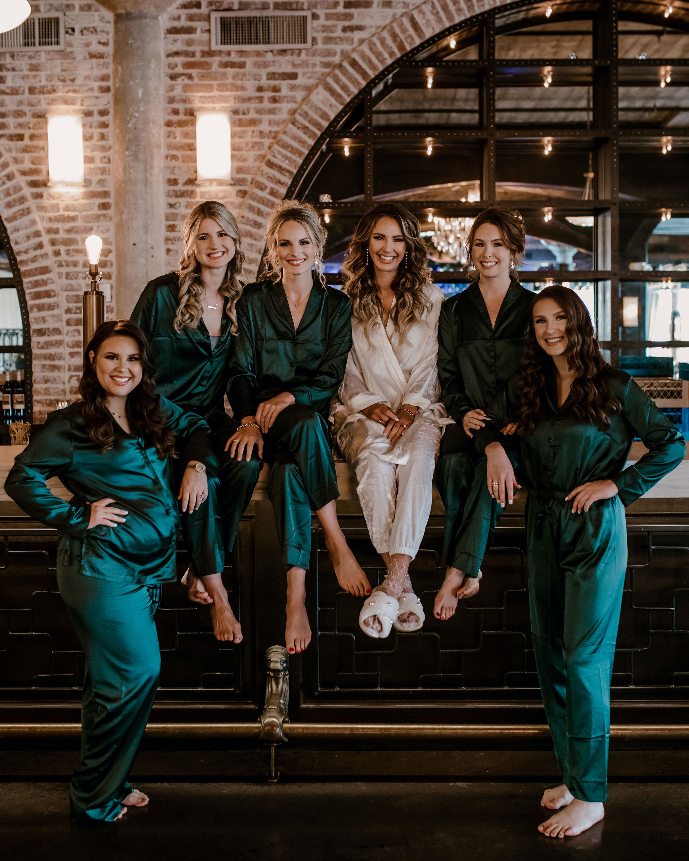 A bride sits with her bridesmaids before her wedding at The Astorian in Houston,TX. The bridesmaids all wear satin green pajamas.