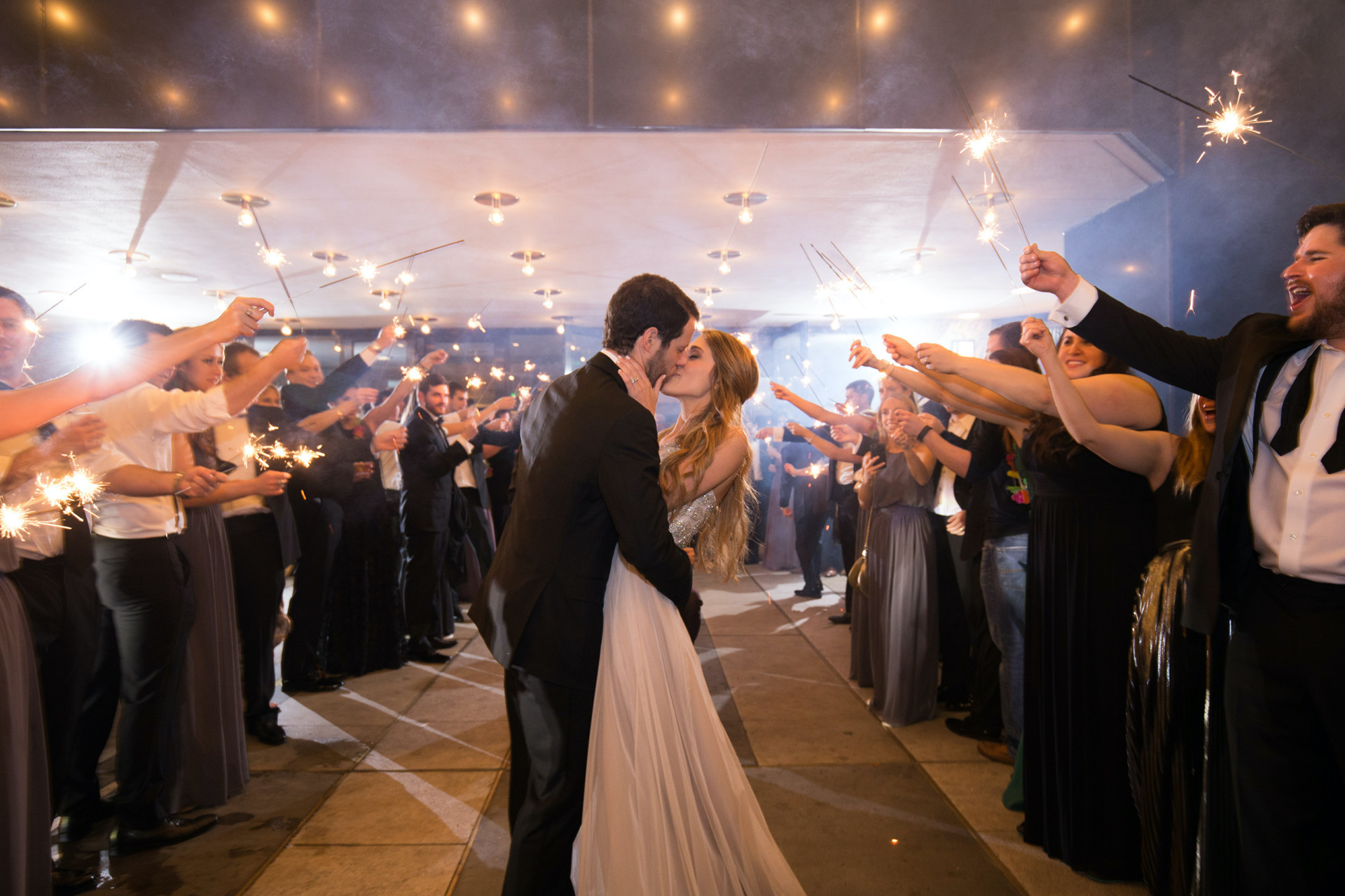 A bride and groom kissing at their wedding send off at Four Seasons Houston. Their guests have sparklers lit around them.