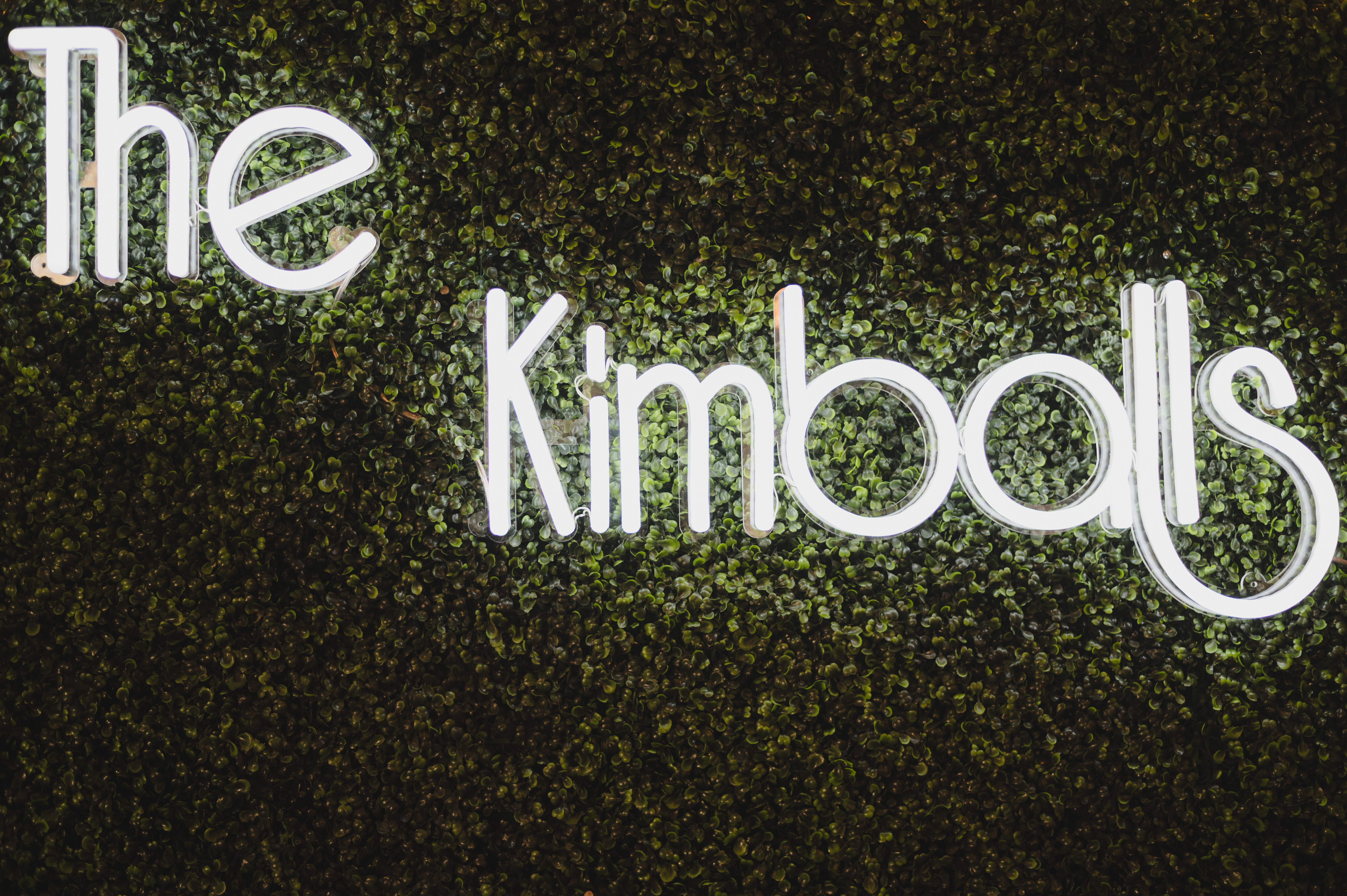 A neon sign on a grass wall that says "The Kimballs" for Jordan and Christina Kimball's wedding in Houston, TX.