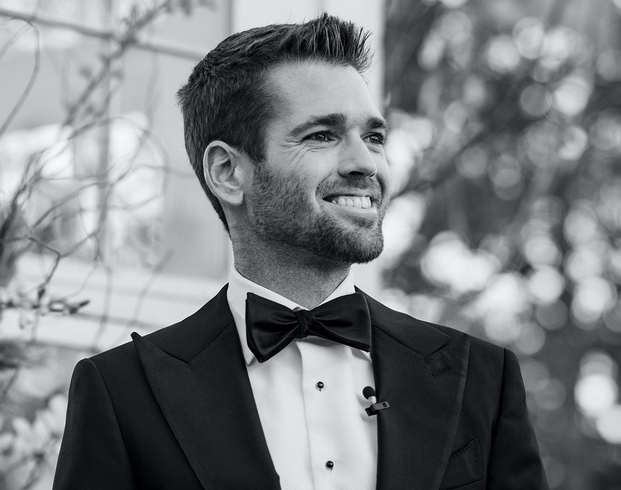 A black and white photo of the groom smiling outside at the altar at his winter wedding at 7F Lodge in College Station, TX.