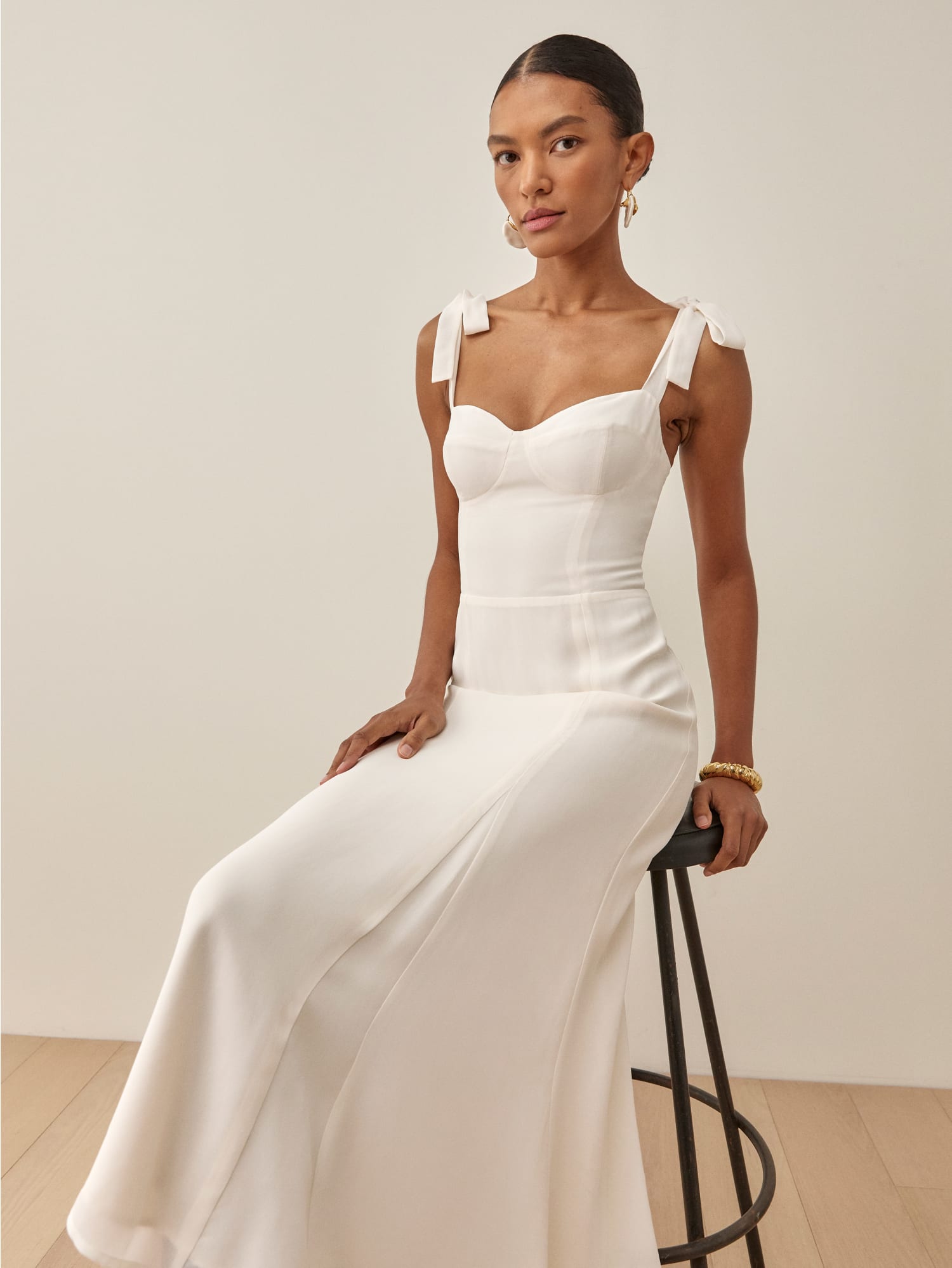 A white midi dress with bowtie straps and a sweetheart neckline for a bride. The dress is from Reformation.