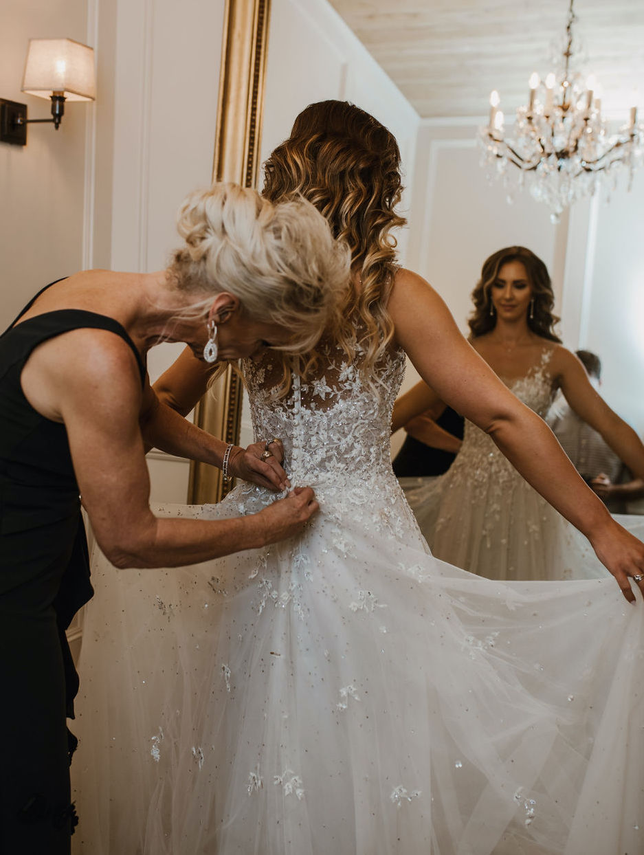 A bride's mom helps her button the back of her wedding dress for her wedding at The Astorian in Houston, TX