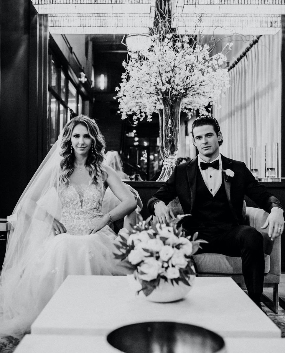 The bride and groom sit on a couch at their wedding venue, The Astorian in Houston, Texas.