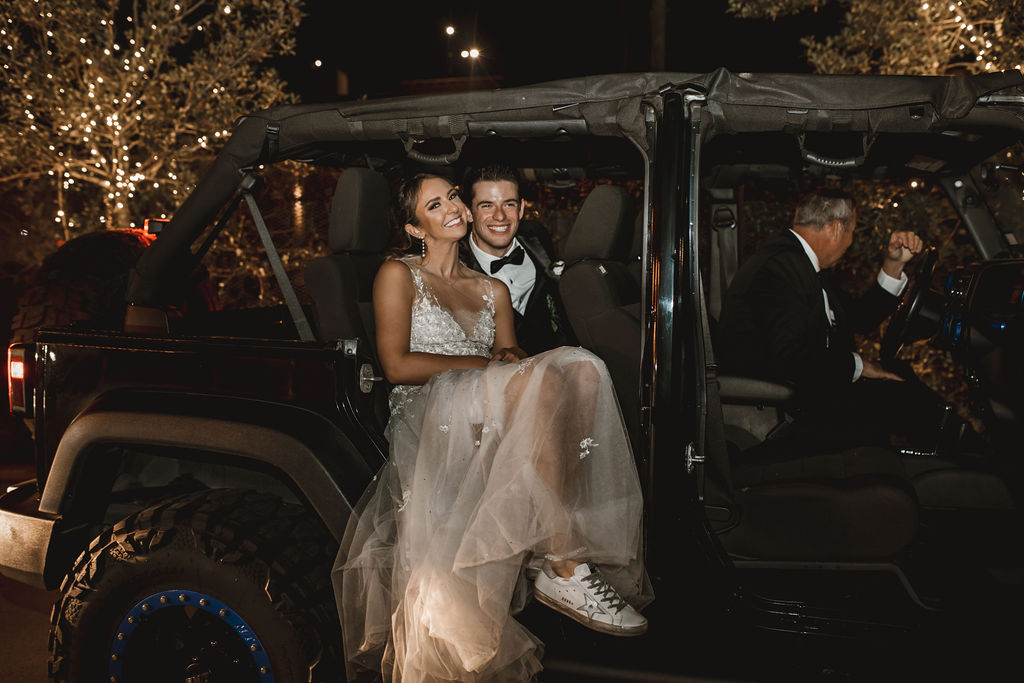 The bride and groom are sitting in a black jeep with the doors and top off as they drive away from their wedding at The Astorian in Houston, Texas and head to their Florida honeymoon.
