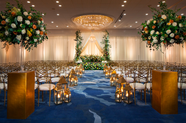 A wedding ceremony is set up at The Westin Galleria Houston with gold accents, lanterns and white and peach flowers.