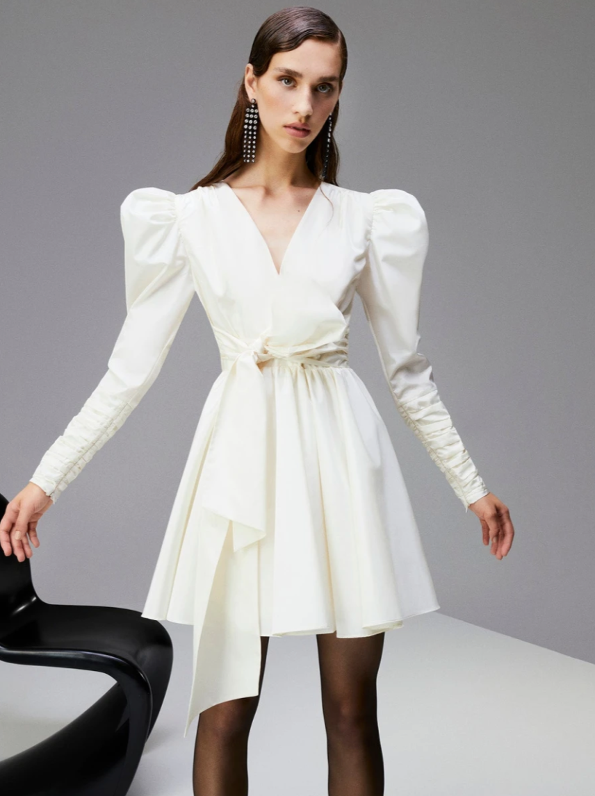 White long-sleeve mini dress with puff sleeves and a bow tie in the front with an a-line skirt. Sold at Wolf & Badger for brides for their bridal shower.