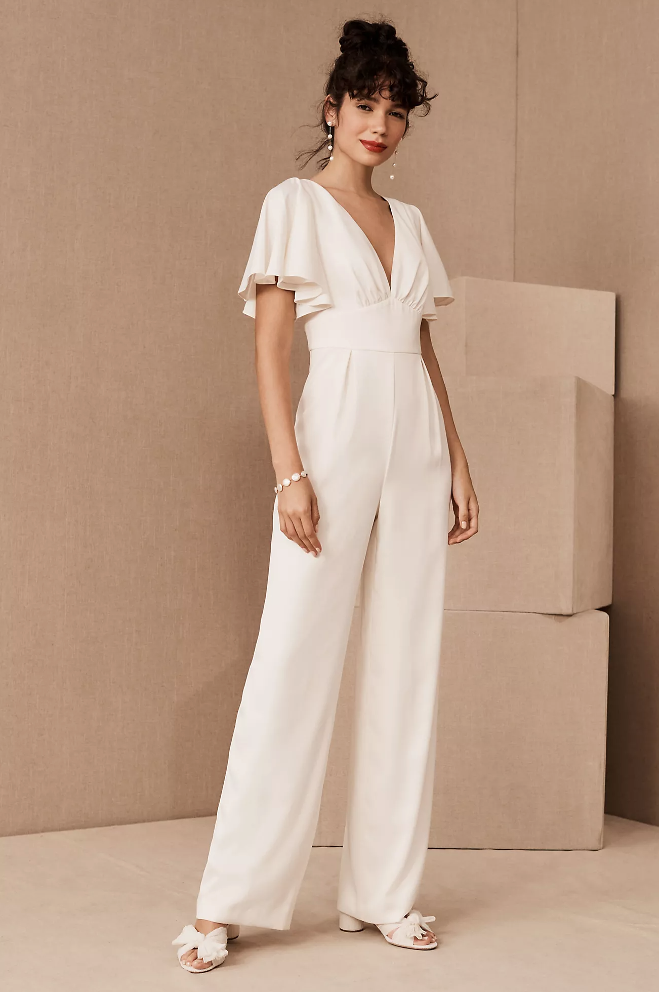 A white jumpsuit with flowy short sleeves and a v-neckline. Sold for brides at Anthropologie BHLDN.