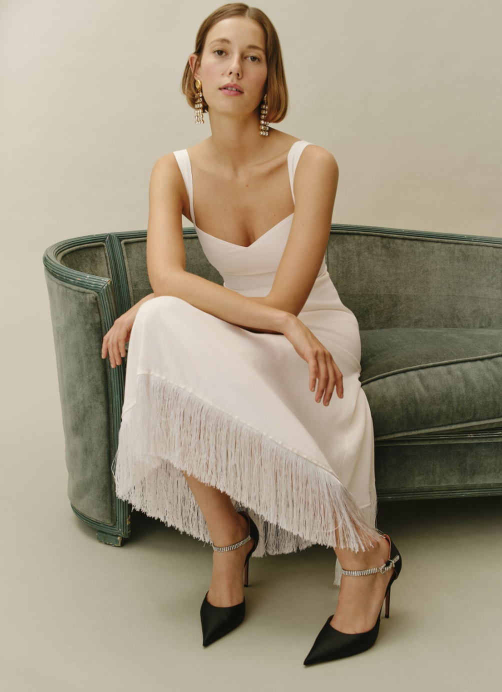 A white midi dress for a bride with a sweetheart neckline and fringe at the hem of the dress. Sold at Reformation and called the sarabeth dress.
