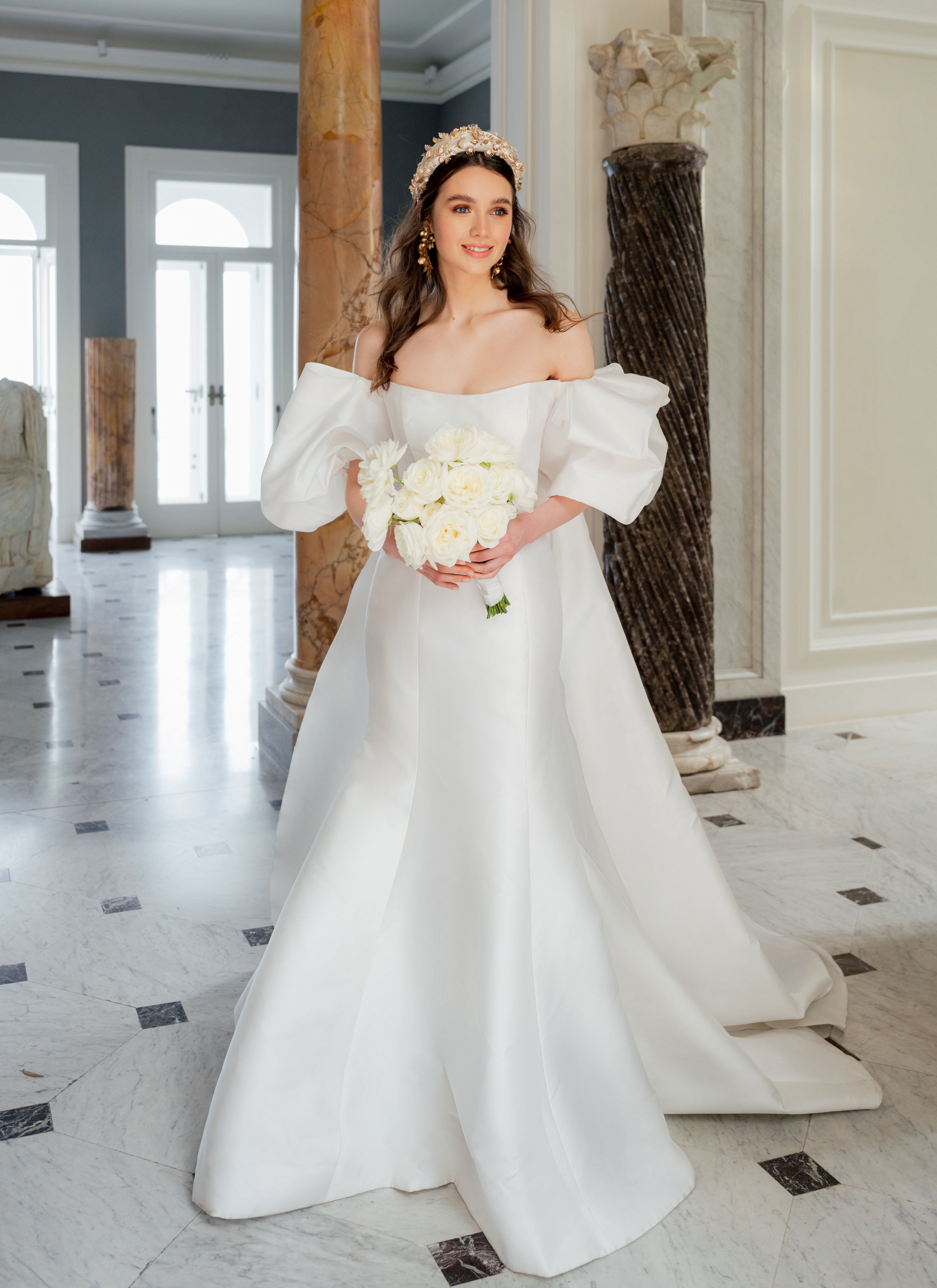 A bride wears a Monique Lhuillier gown and holds a bouquet of white roses to meet her groom.