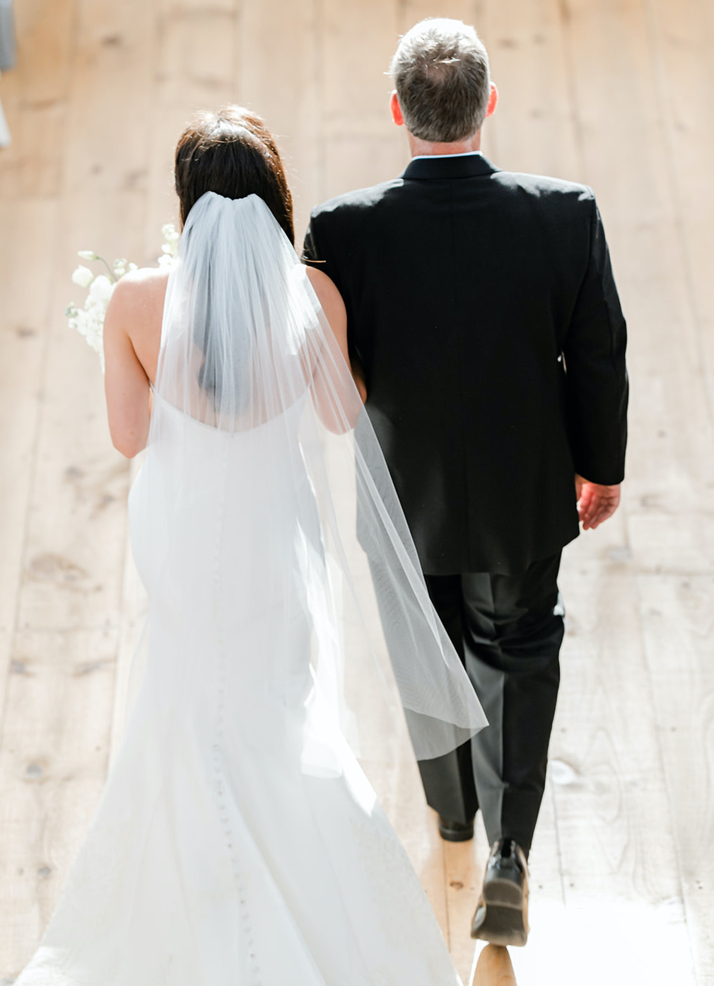 A bride walks down the aisle with her father at her elegant summer wedding.