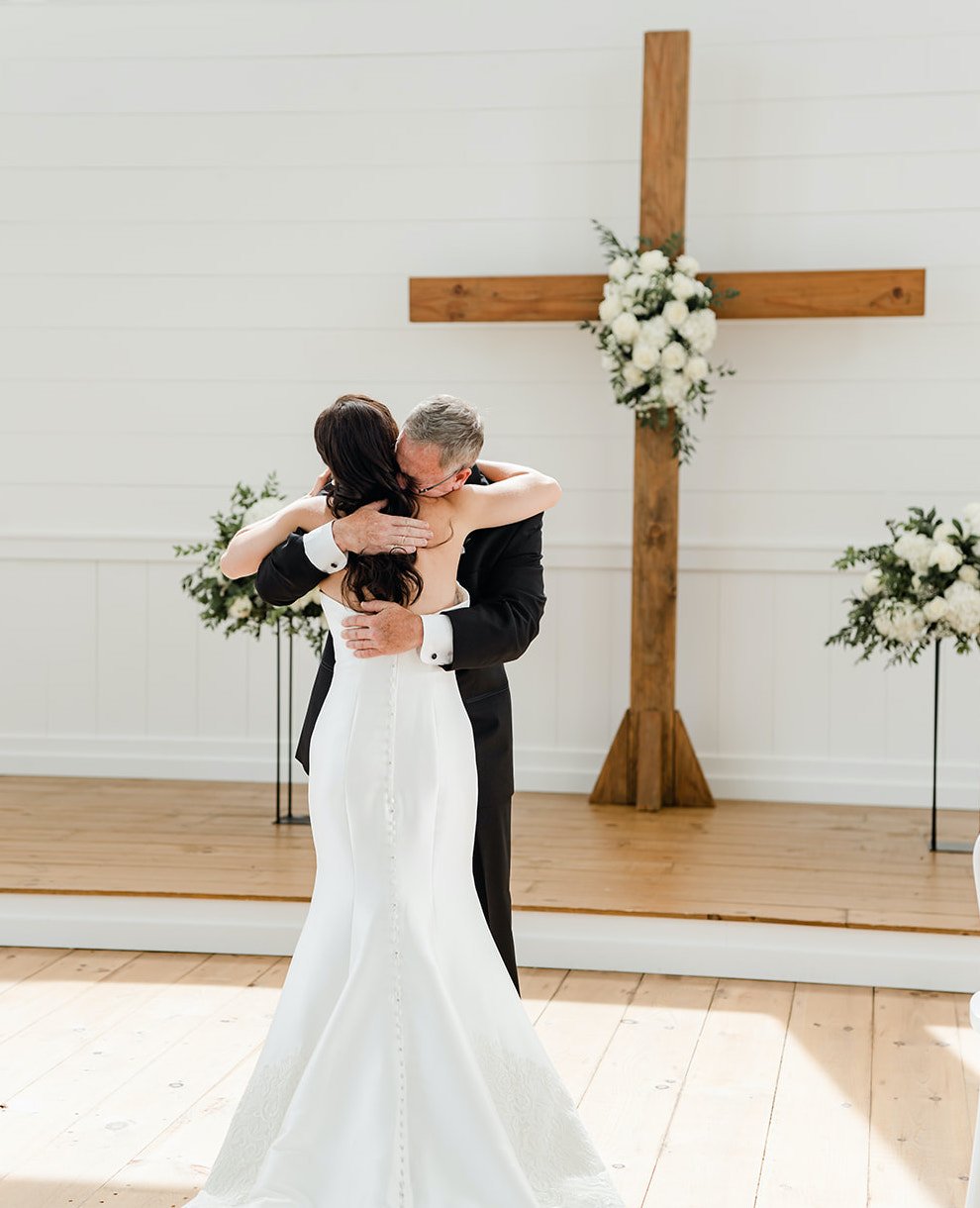 A bride and her dad hug in front of the altar before her wedding.