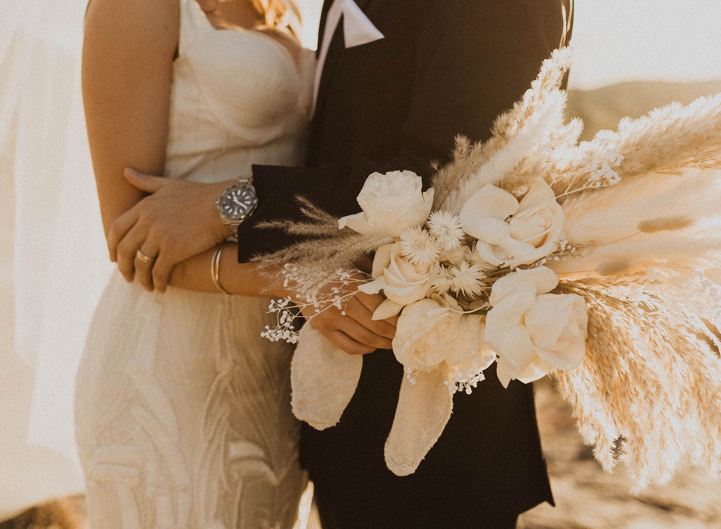 A bride holds a bohemian bridal bouquet with white roses and dried flowers.