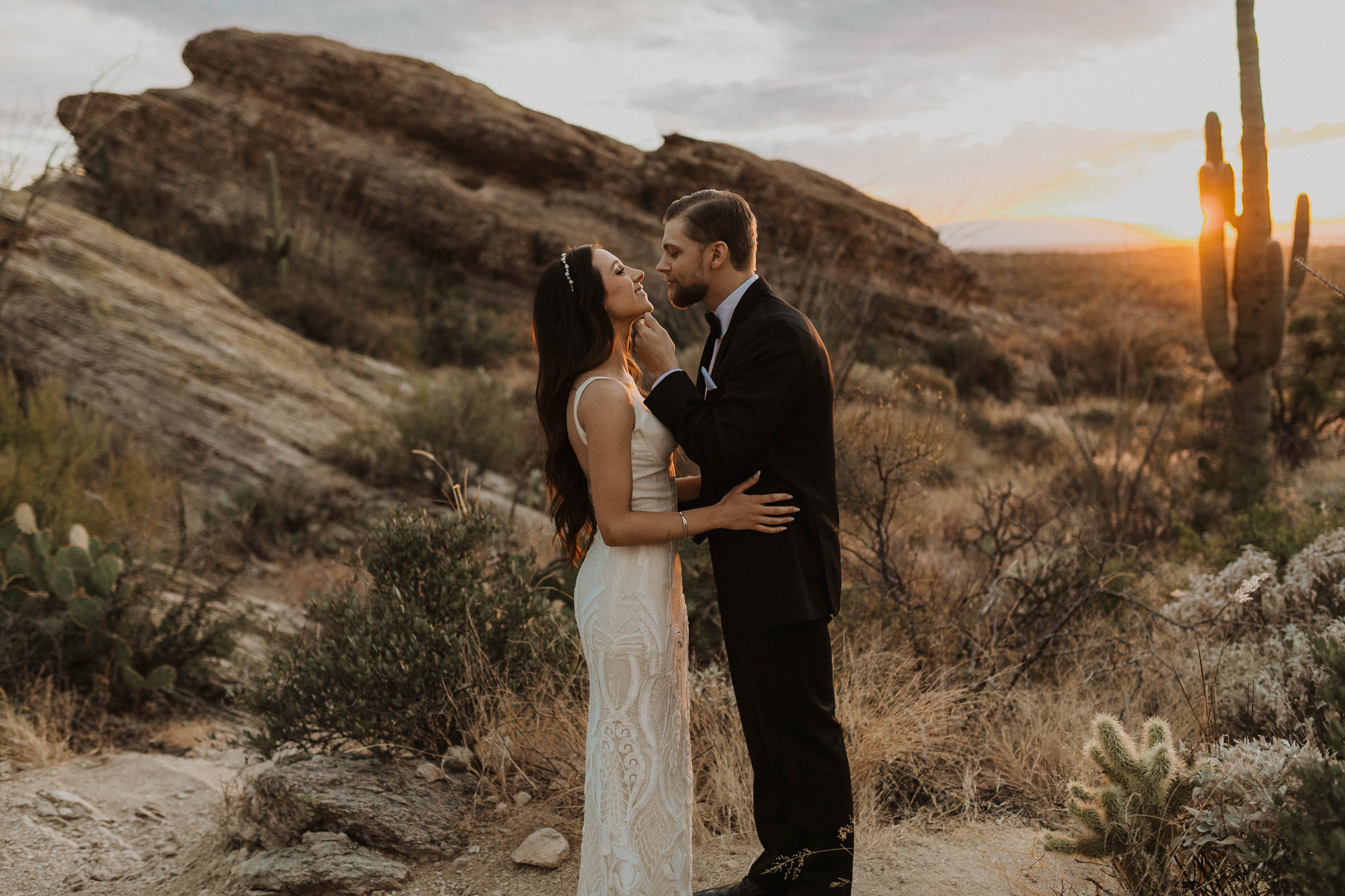 Bride and groom look at each other as the sun sets behind them in the Arizona desert.