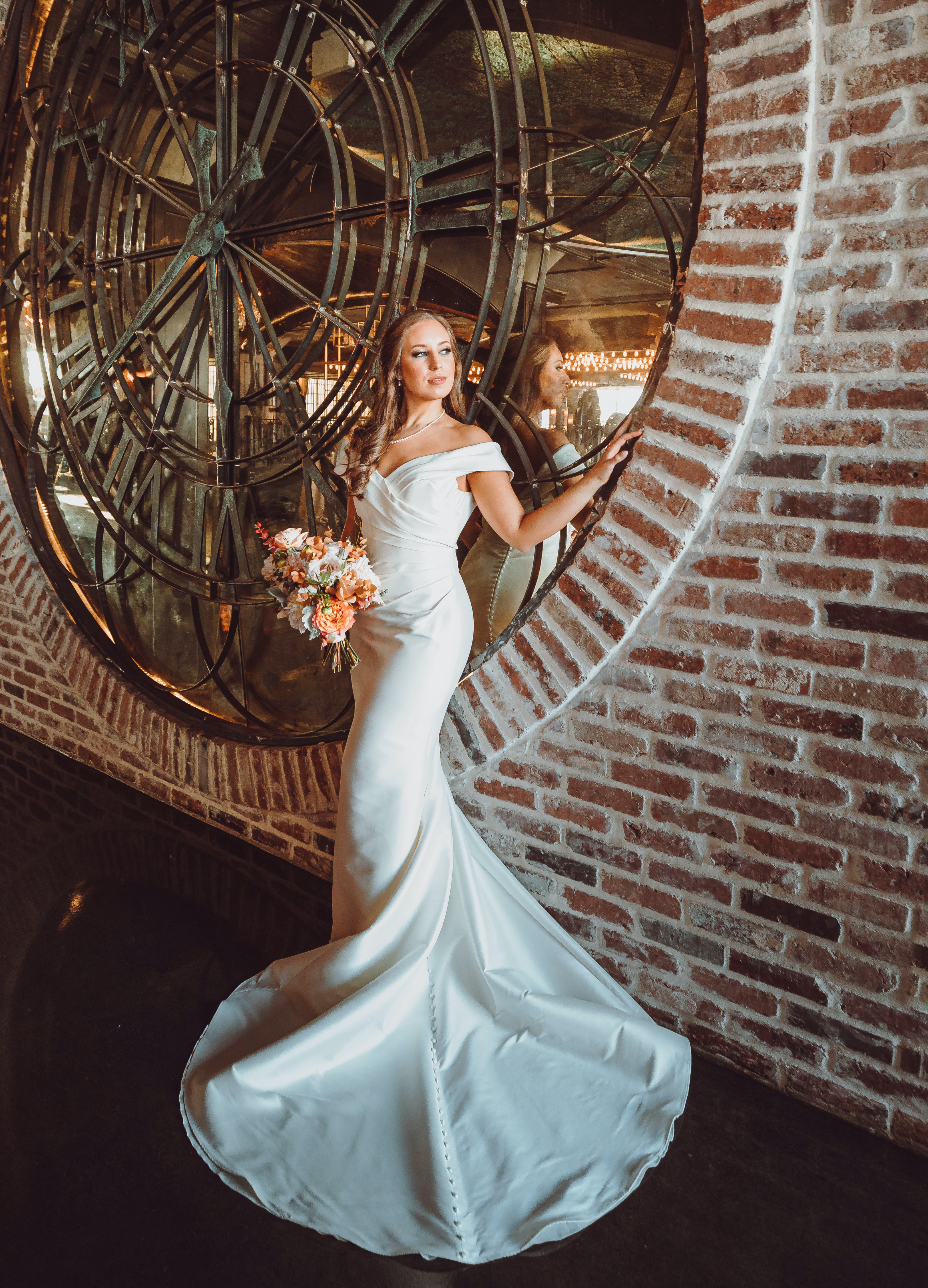 A bride stands by a historic clock in The Astorian while holding her bridal bouquet.