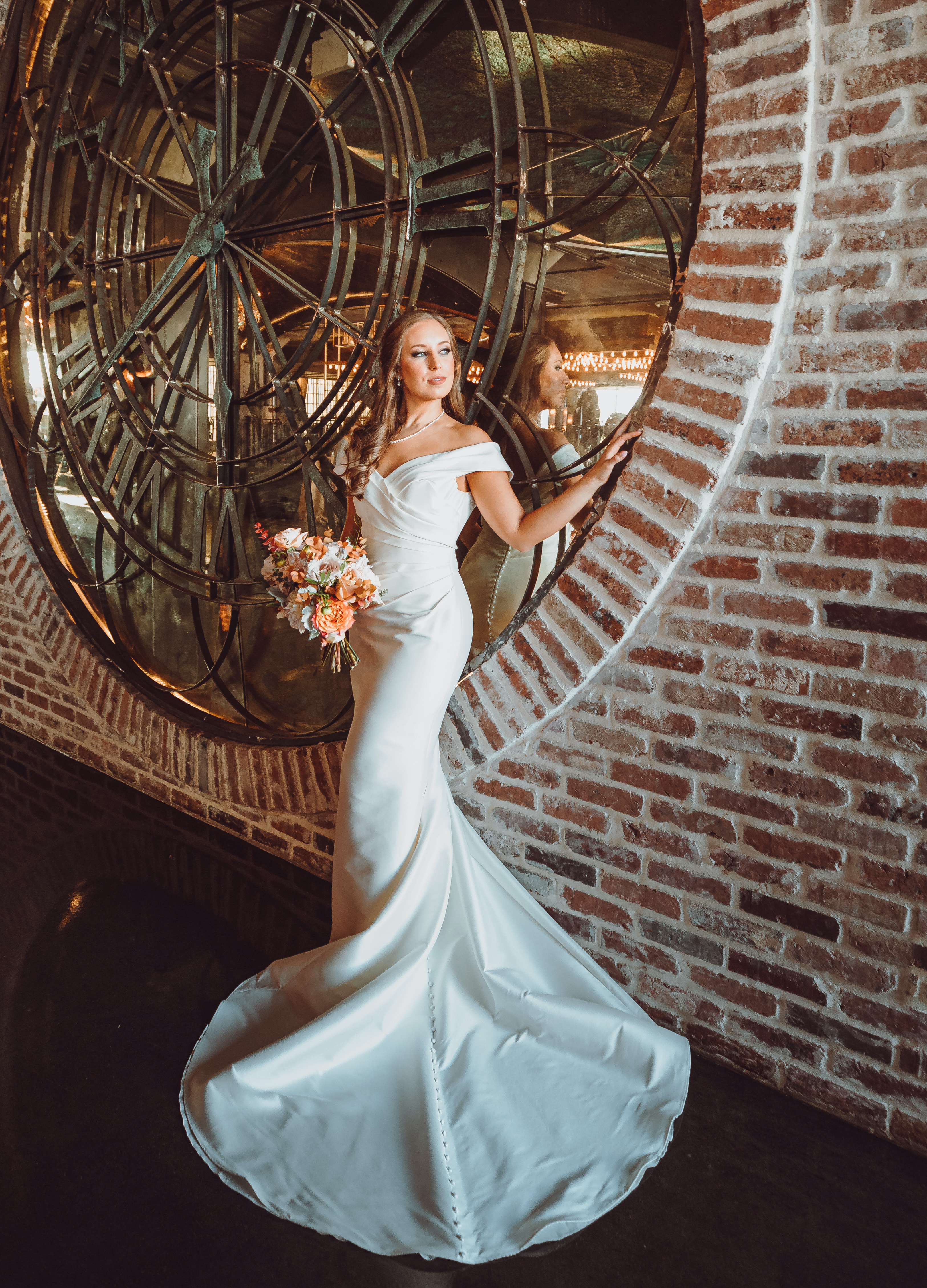 A bride stands by a historic clock in The Astorian while holding her bridal bouquet.