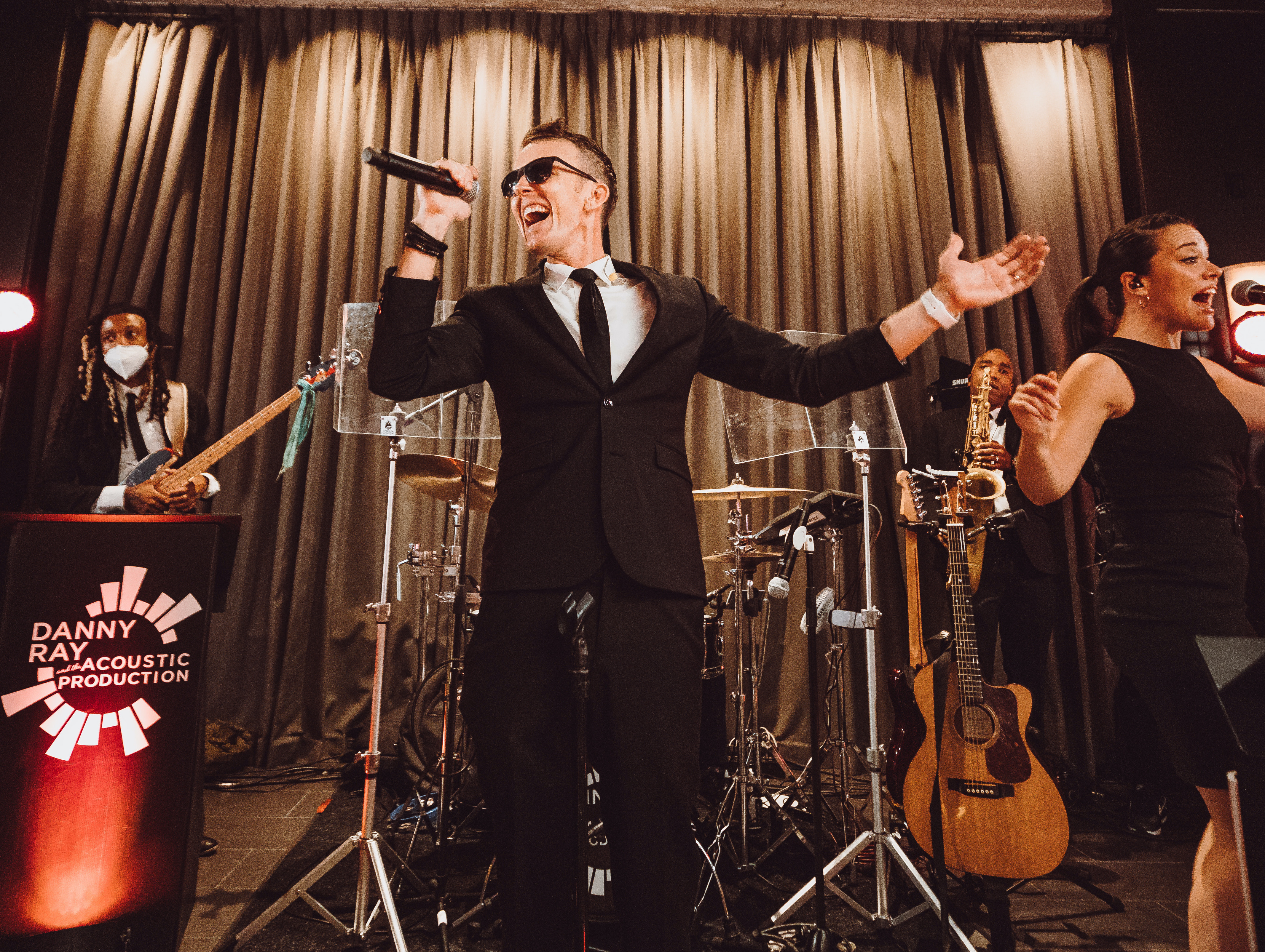 Danny Ray of Danny Ray and The Atlantic Street Band sings with a microphone next to a female singer and a male bass player at a fall wedding at The Astorian in Houston, Texas. 