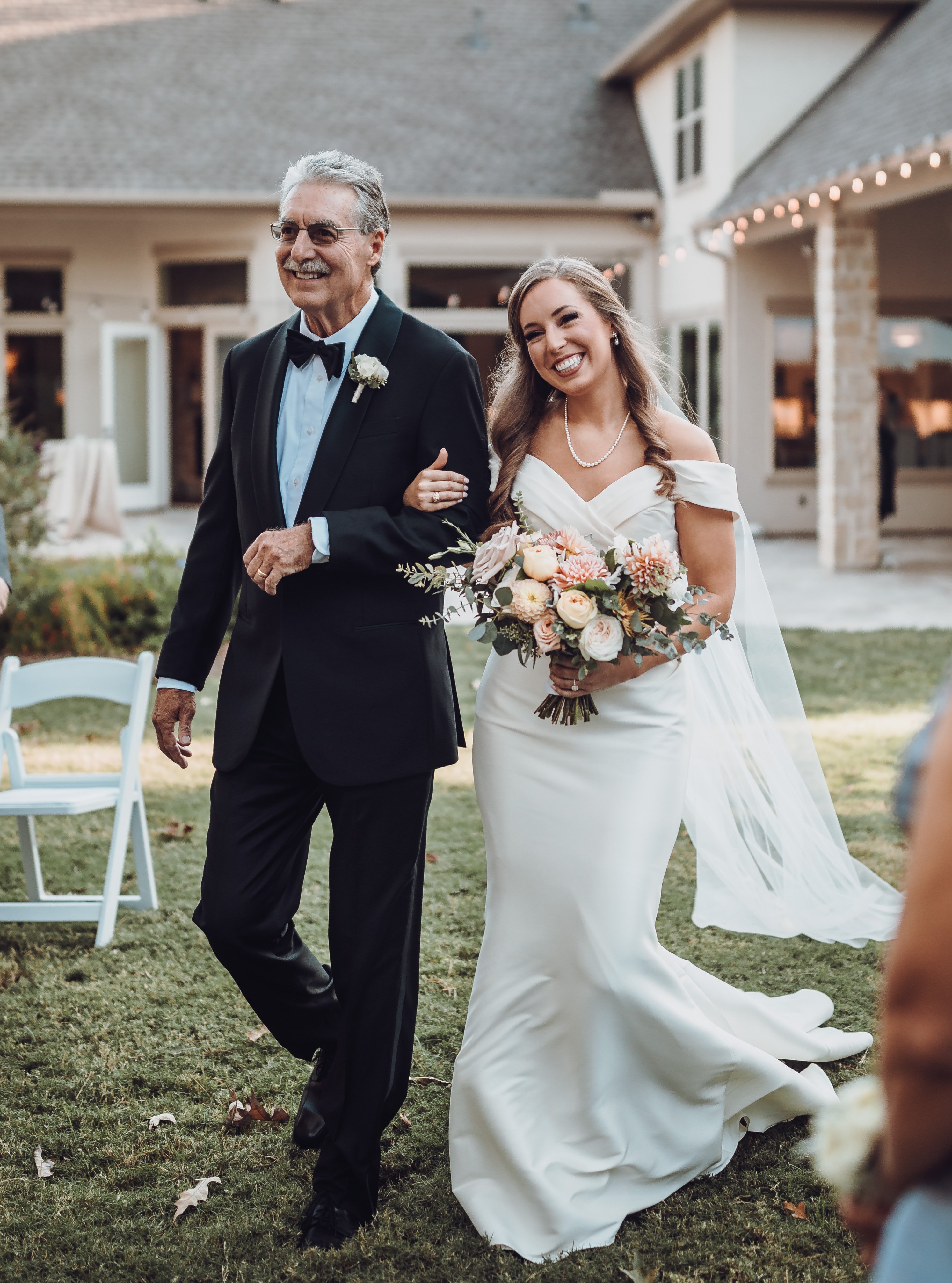 A bride smiles while walking down the aisle with her dad by her side.