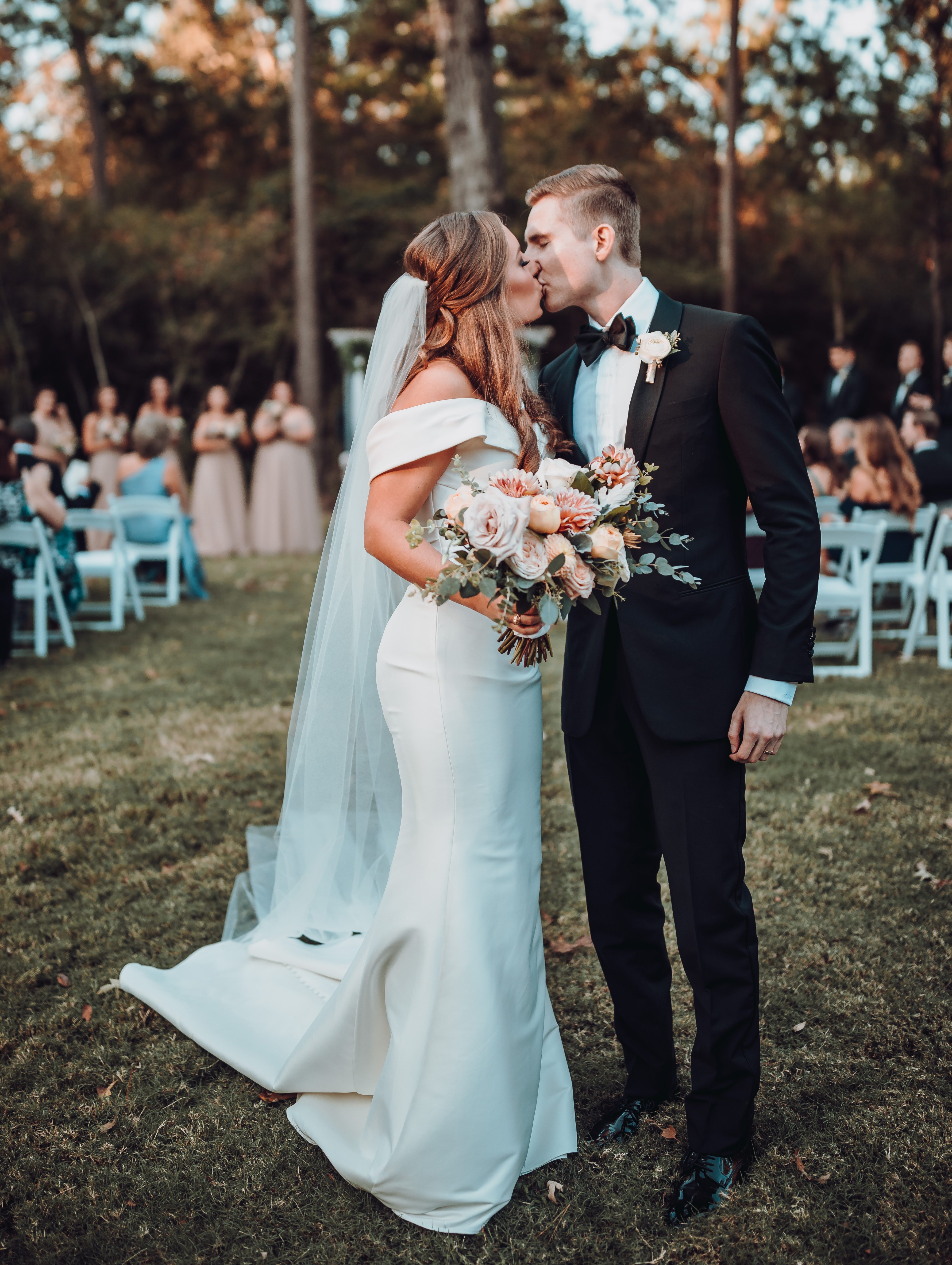 Bride, holding dusty pink and orange bouquet, kisses her new husband at an intimate backyard wedding ceremony photographed by Ama by Aisha. 