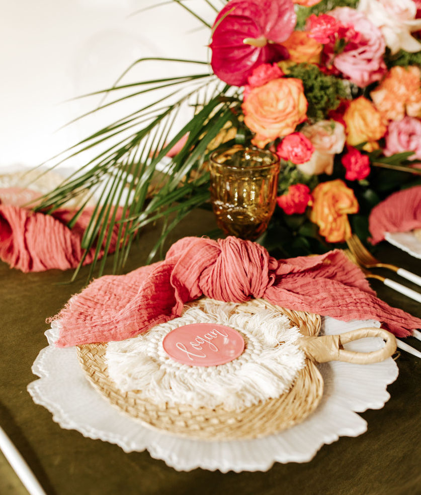 Tropical Havana wedding inspiration: a reception table setting with a rattan fan and tropical pink and orange flowers.