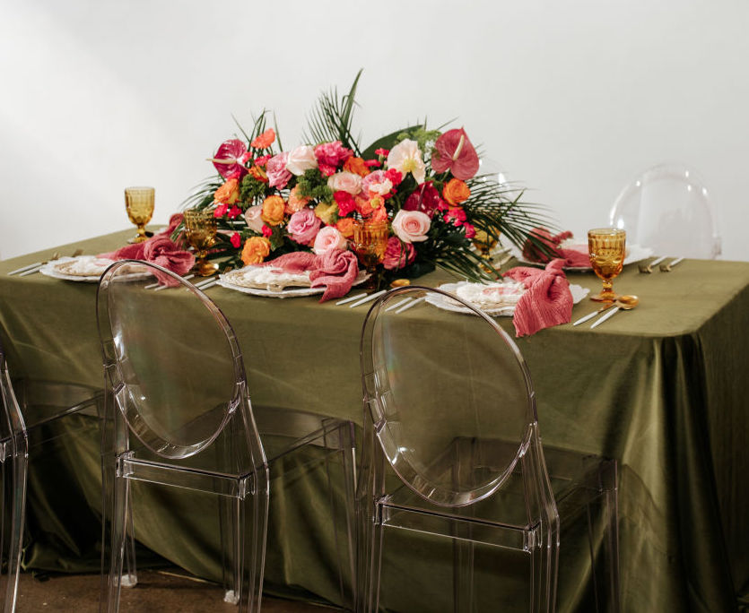 A wedding reception table with a velvet green runner and vibrant pink and orange tropical wedding flowers as the centerpiece.