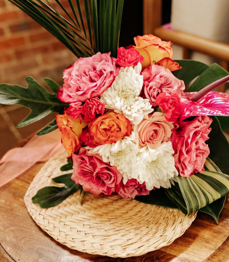 A vibrant pink and orange bridal bouquet with tropical palms.