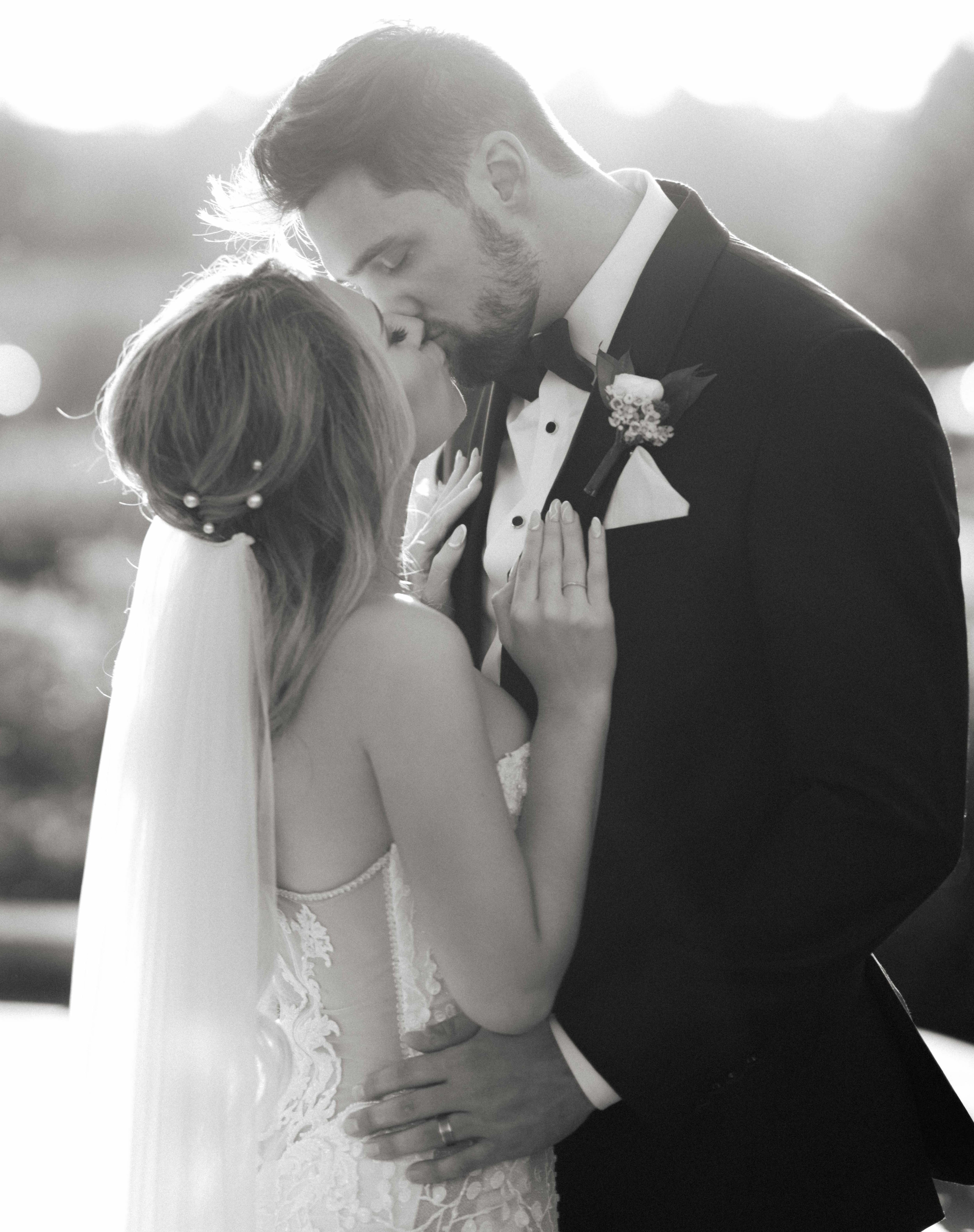 A black and white photo of a bride and groom kissing outside after their wedding ceremony in Conroe, TX.