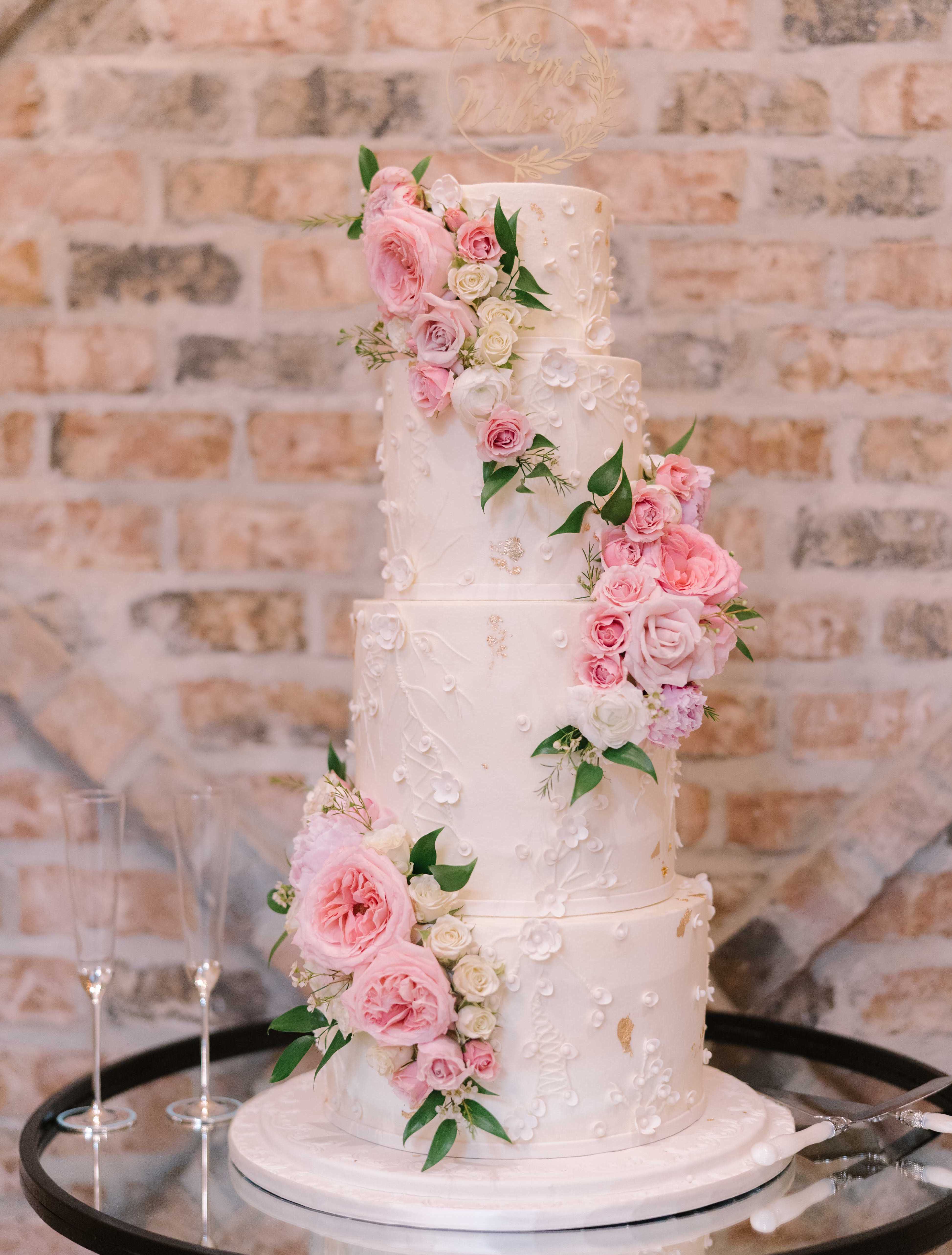 A four-tier white wedding cake with 3D floral embellishments and pink cake flowers trailing up the sides. Summer Wedding With a Vibrant Palette of Pink