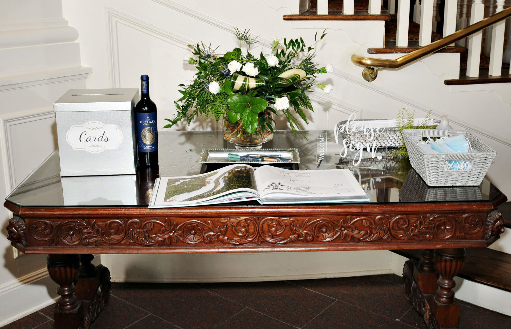 A welcome table has a greenery-filled centerpiece and a guest book for a wedding at The Tremont House Hotel in Galveston, TX.