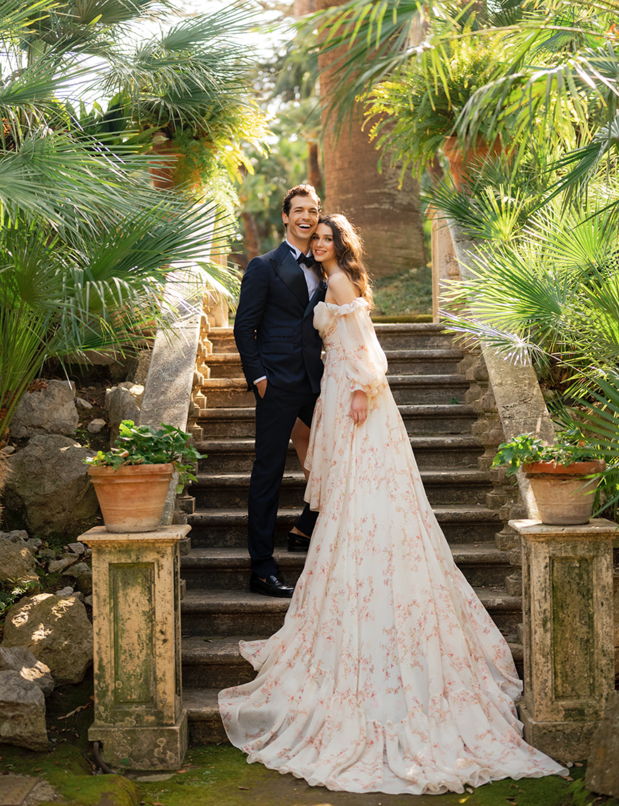 A bride and groom stand on outdoor stairs and smile while the sunlight hits their faces at their wedding venue in Amalfi Coast, Italy.