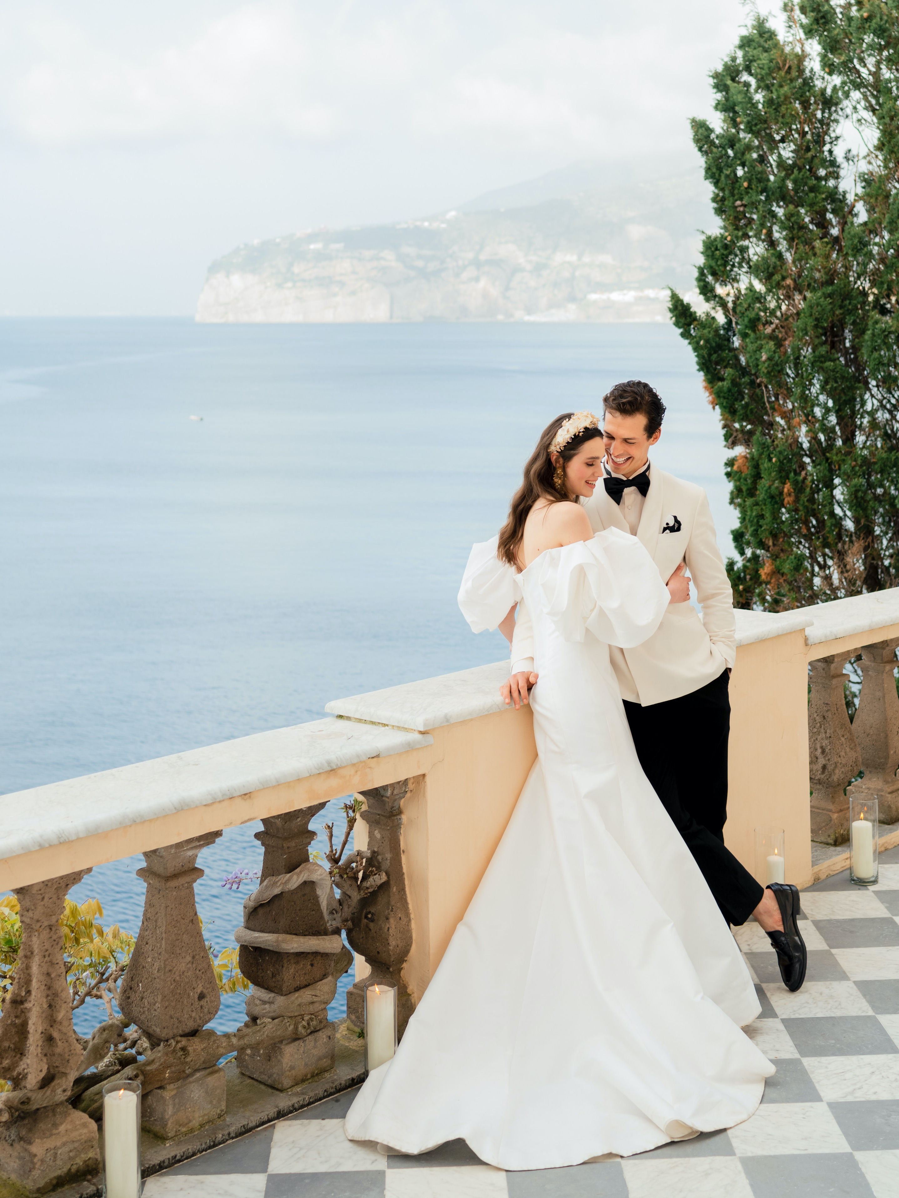 A bride and groom stand near a balcony ledge that overlooks the sea in Amalfi Coast, Italy.
