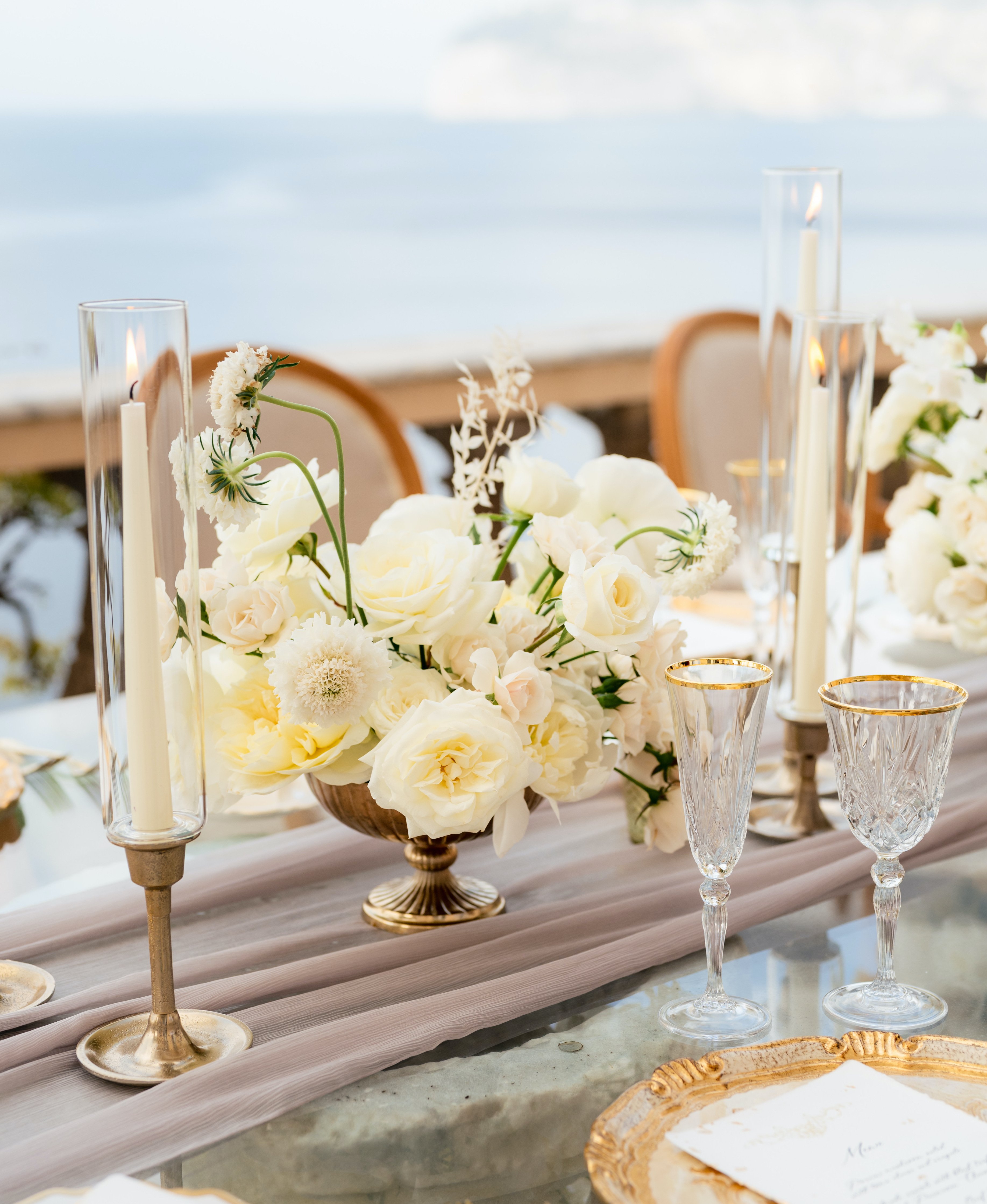 Beautiful gold compotes are full of white flowers for centerpieces at an alfresco wedding reception on the Amalfi Coast.