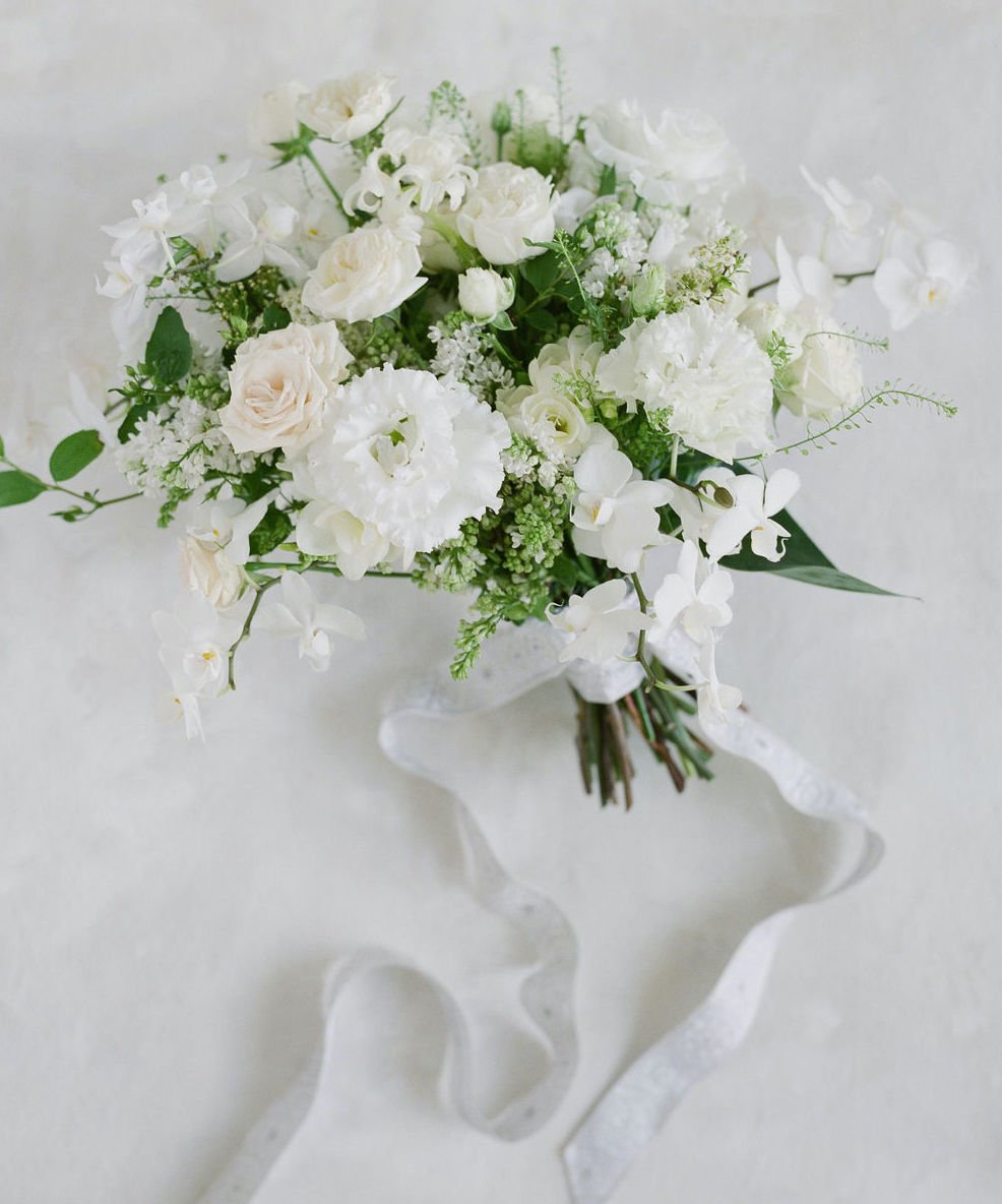 An all white bridal bouquet with a white ribbon tied around the base.