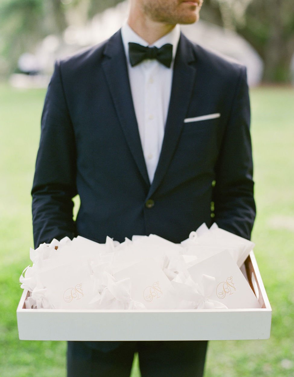 A man is holding a tray of white wedding booklets for guests.