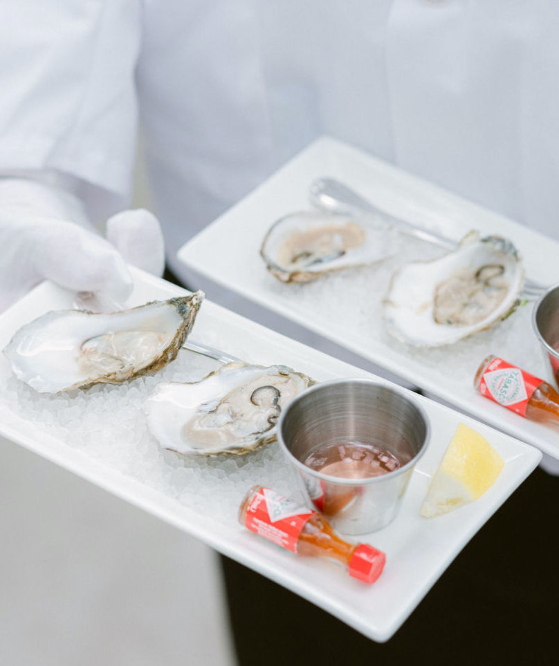 Fresh oysters are placed over ice with mini Tabasco hot sauce bottles for wedding guests.