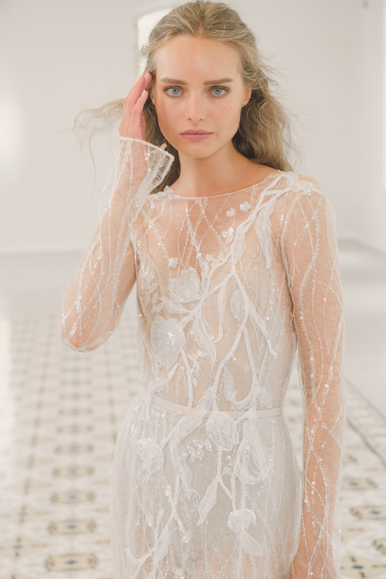 A sheer long sleeve wedding gown designed by Mira Zwillinger with shimmering flowers and a slim fit.