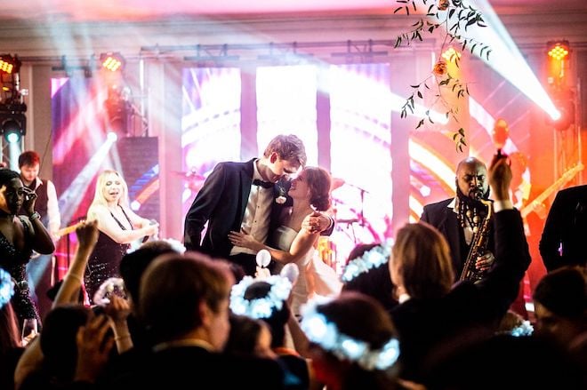 Bride and groom hug each other on a stage at their wedding reception while their wedding band, EastCoast Entertainment, performs.